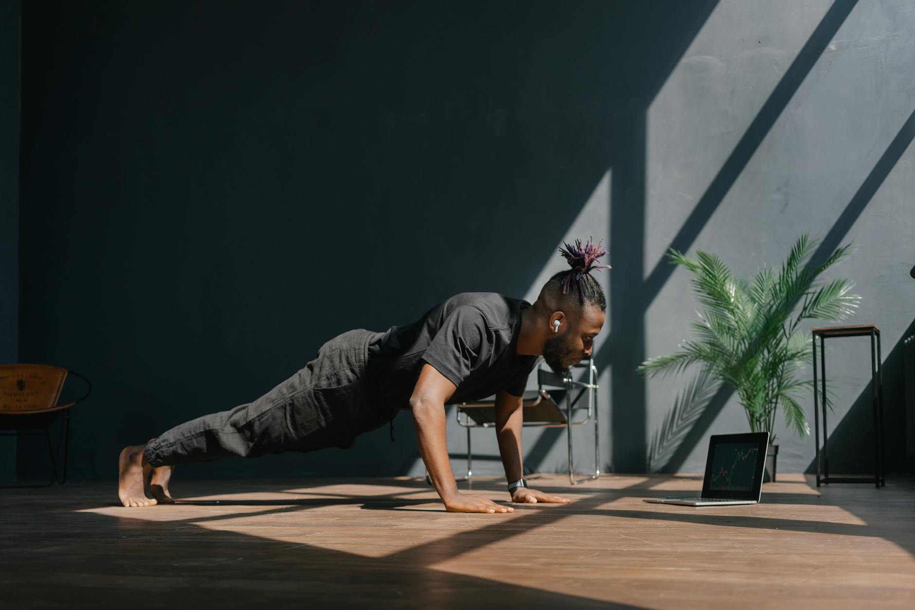 An adult man doing push-ups indoors, guided by a laptop. Fitness and technology merge. - spring bodyweight workout
