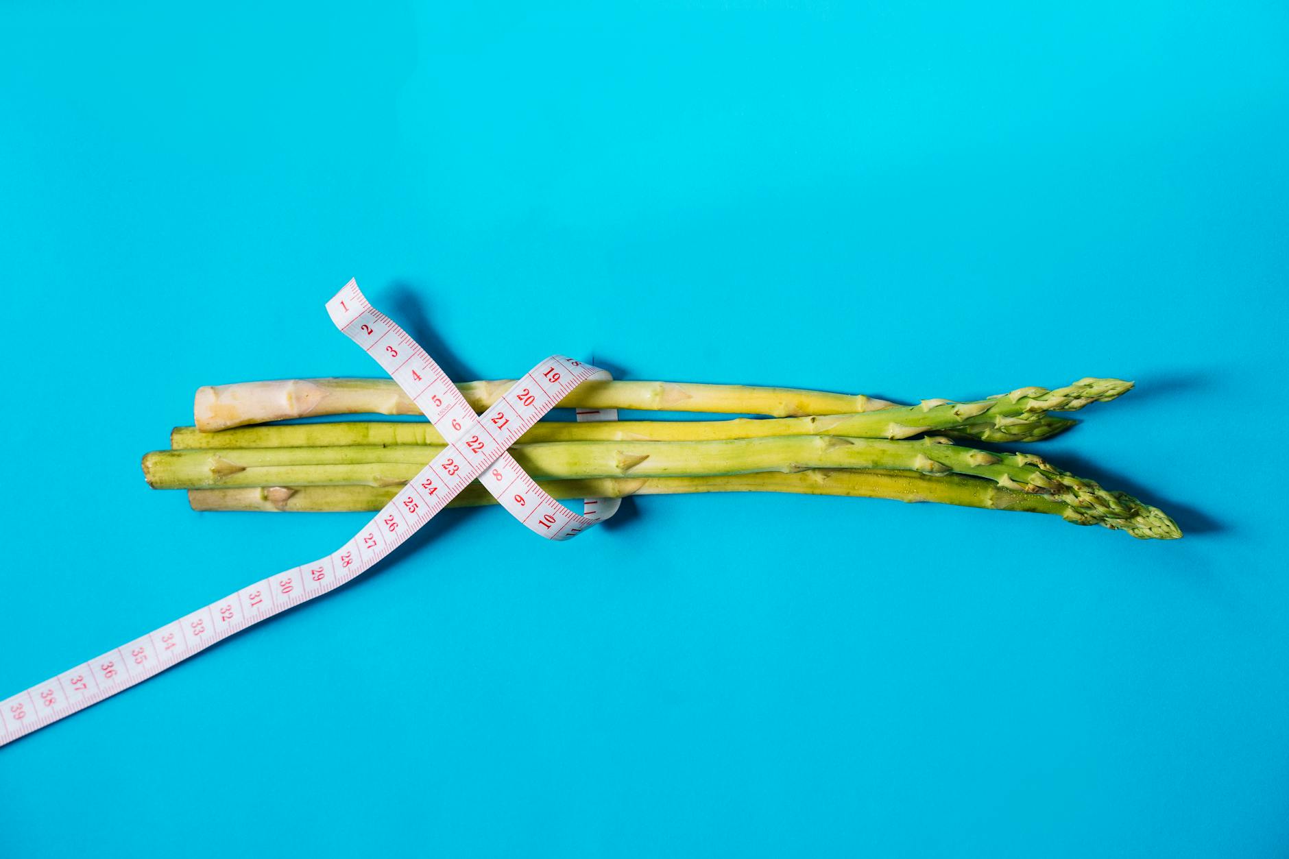 Fresh asparagus wrapped with measuring tape on a vibrant blue background. - spring calorie burning hikes