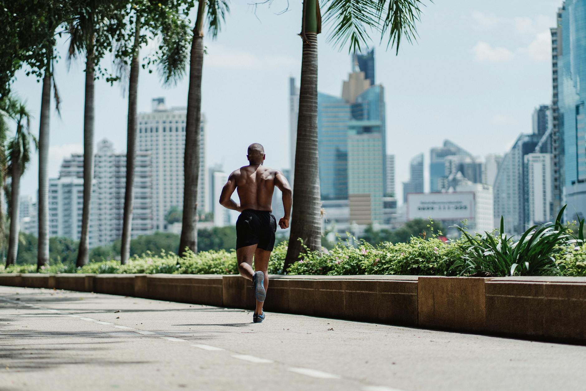 A shirtless man jogging on a sunny day in an urban cityscape with tall buildings. - spring cardio outdoors