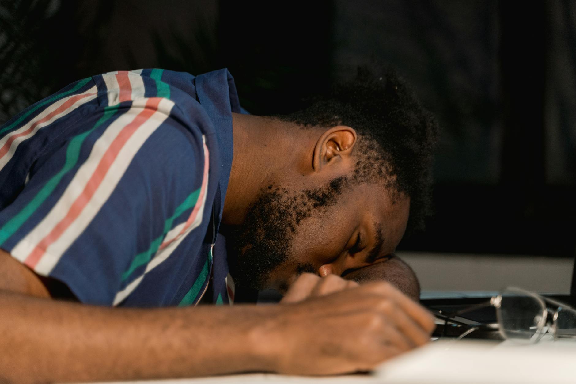 A man with facial hair rests his head on a desk, napping during a late work session. - spring fatigue remedies