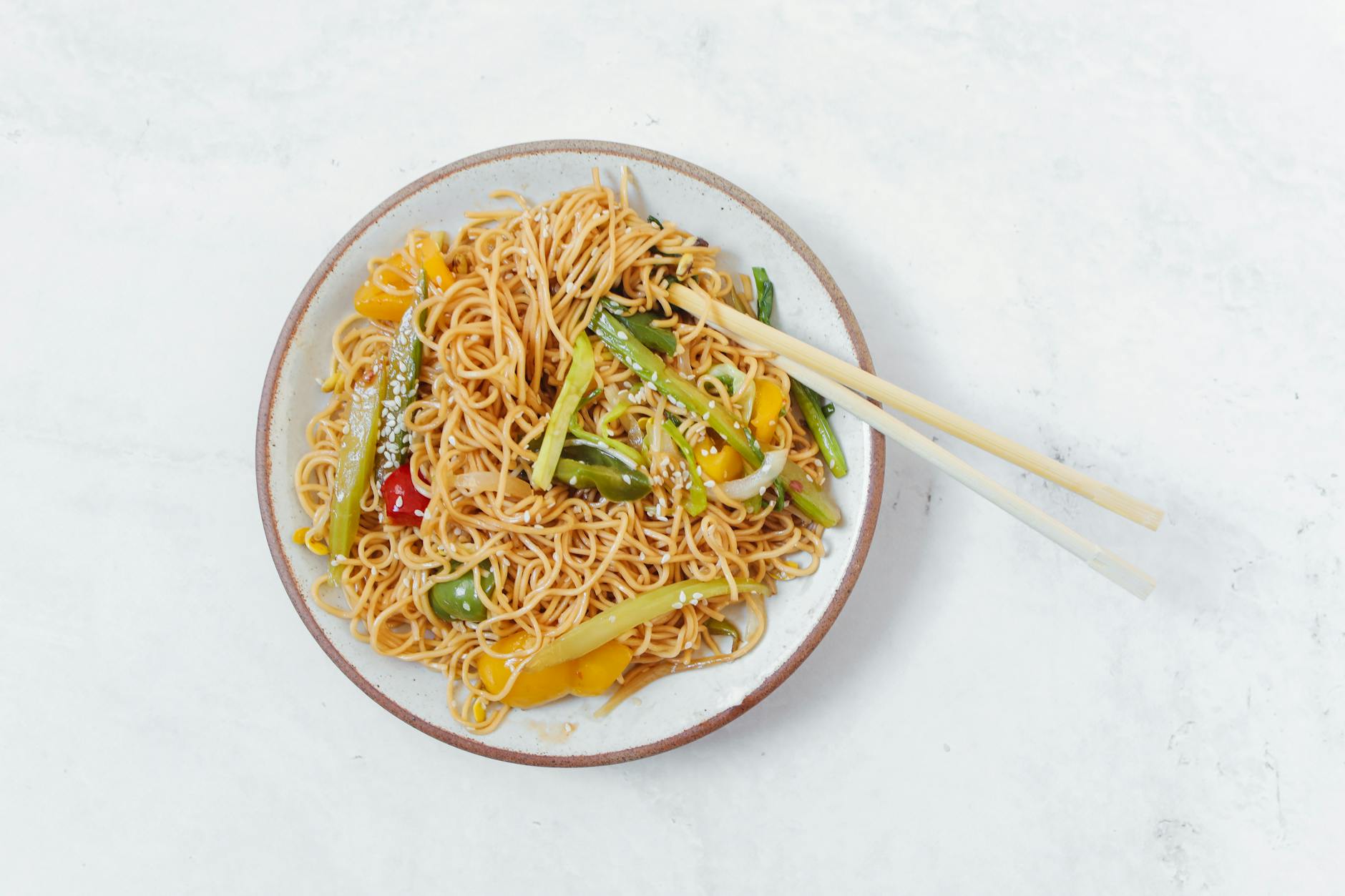 Appetizing plate of stir-fried noodles with colorful vegetables and chopsticks. - spring meal prep