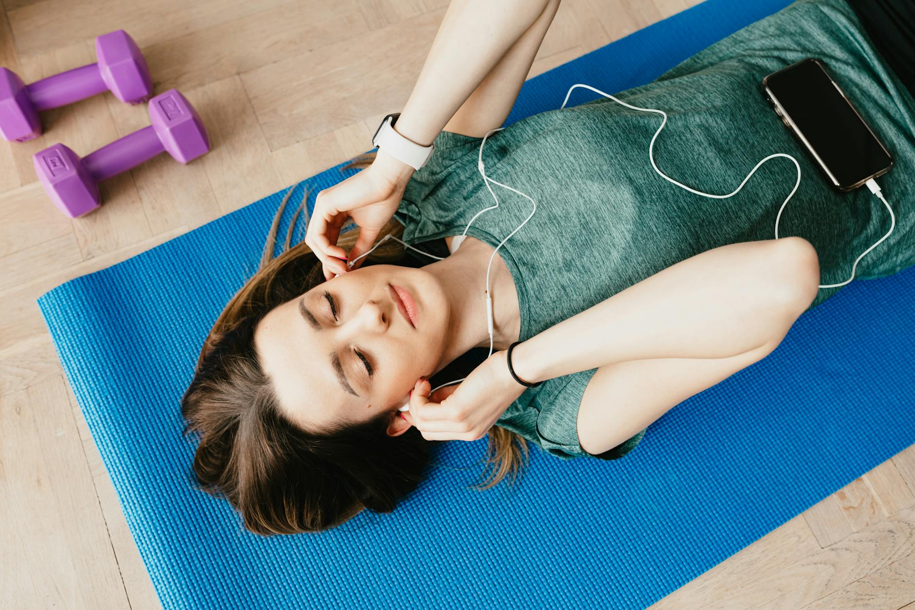 Young woman enjoying music while relaxing on a yoga mat indoors, embodying tranquility and mindfulness. - spring mindfulness stress