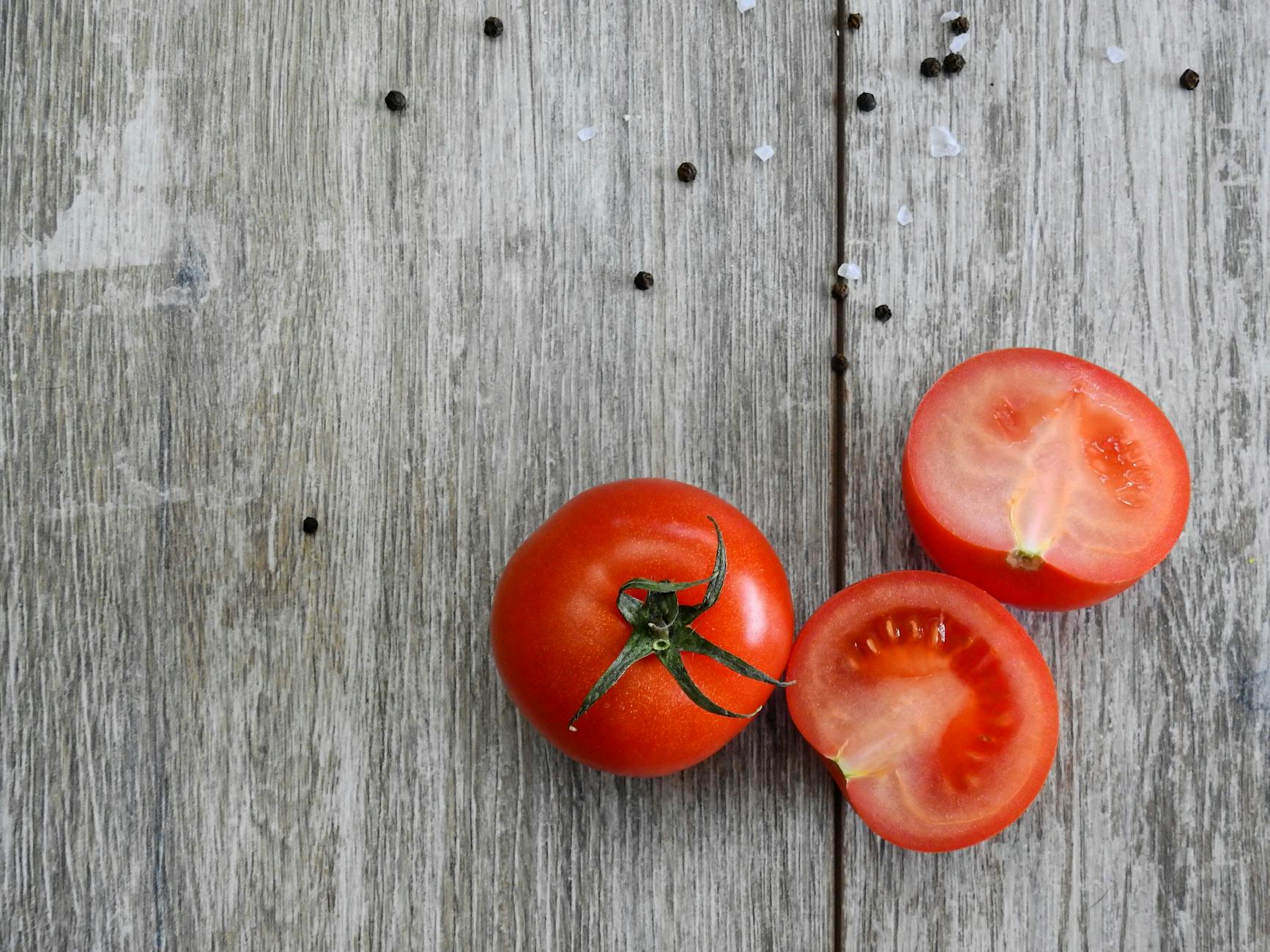Close-up of ripe tomatoes on a rustic wooden table with peppercorns. - spring produce benefits