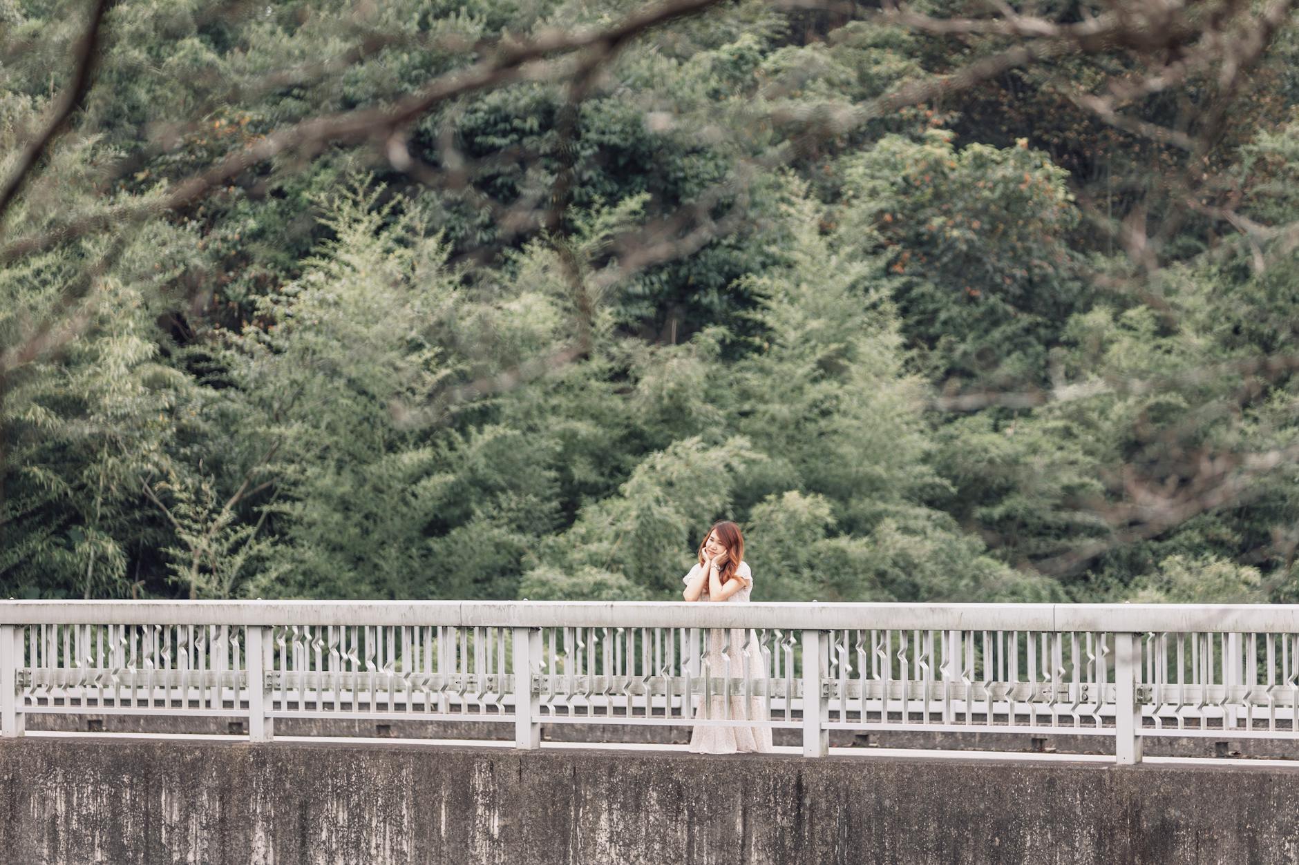 A woman stands on a bridge surrounded by lush greenery, embodying a serene summer vibe. - spring reset challenge