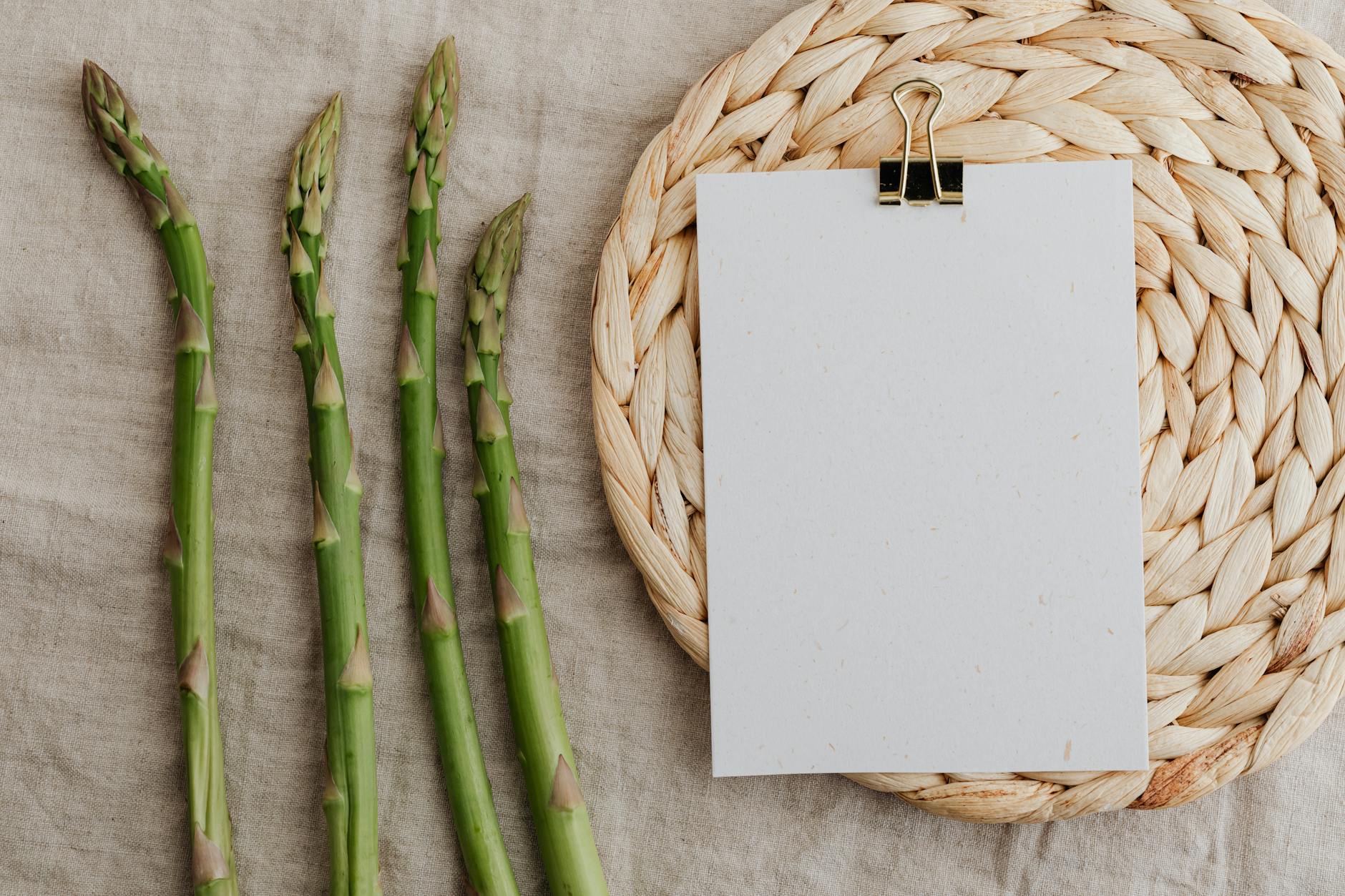 Fresh asparagus arranged on rustic fabric with a blank paper on a woven mat, perfect for culinary themes. - spring vegetable recipes