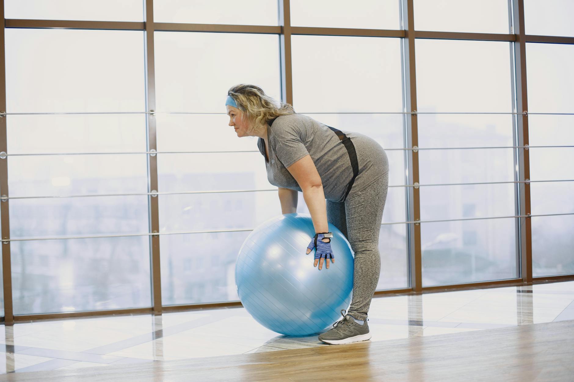 Adult woman working out indoors using a fitness ball by the window. - spring workout plan