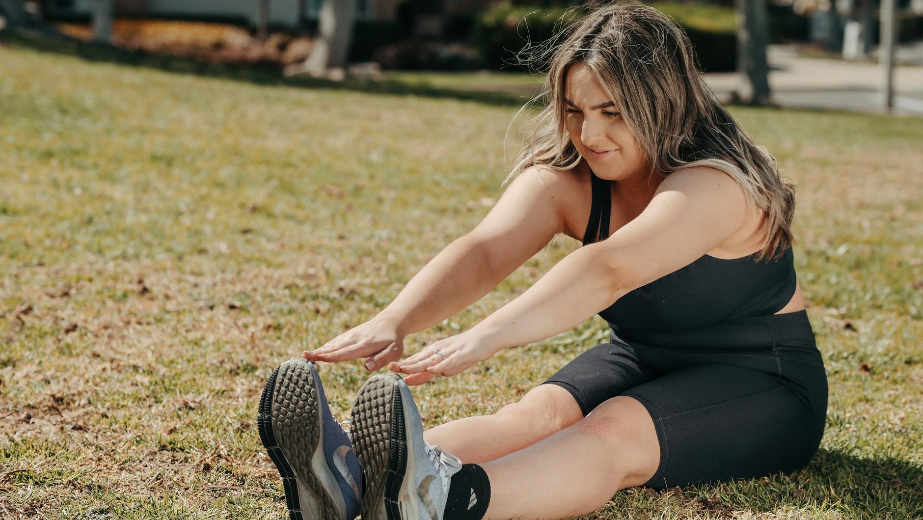 Caucasian woman stretching on grass in athletic wear, enjoying a sunny outdoor workout. - spring workout refresh