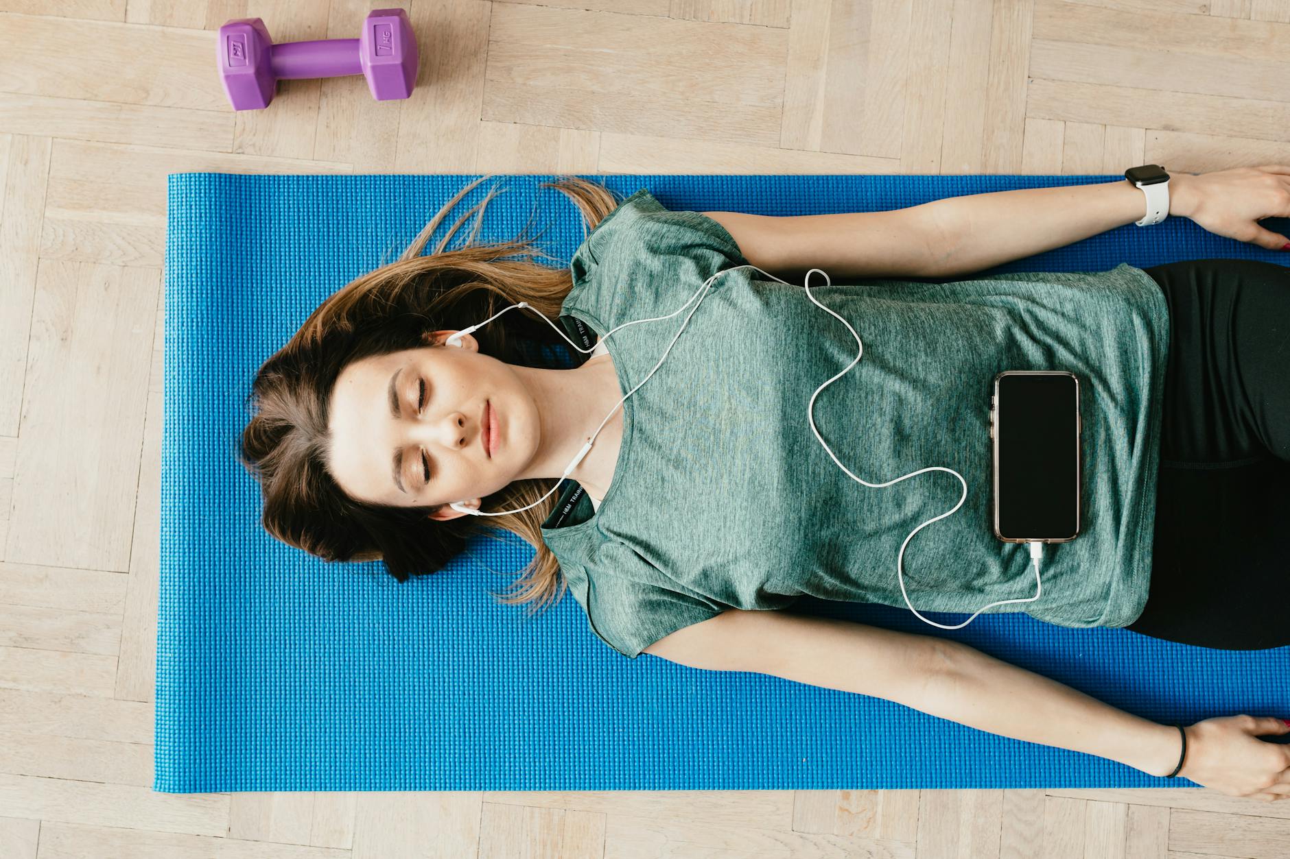 Young woman lying on a yoga mat listening to music for relaxation and mindfulness. - stress relief exercises
