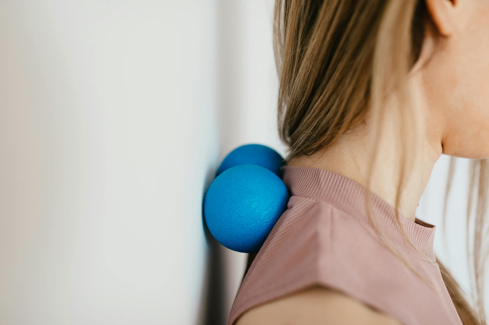 Close-up of woman using blue massage balls for neck relief against a wall. - stress relief exercises