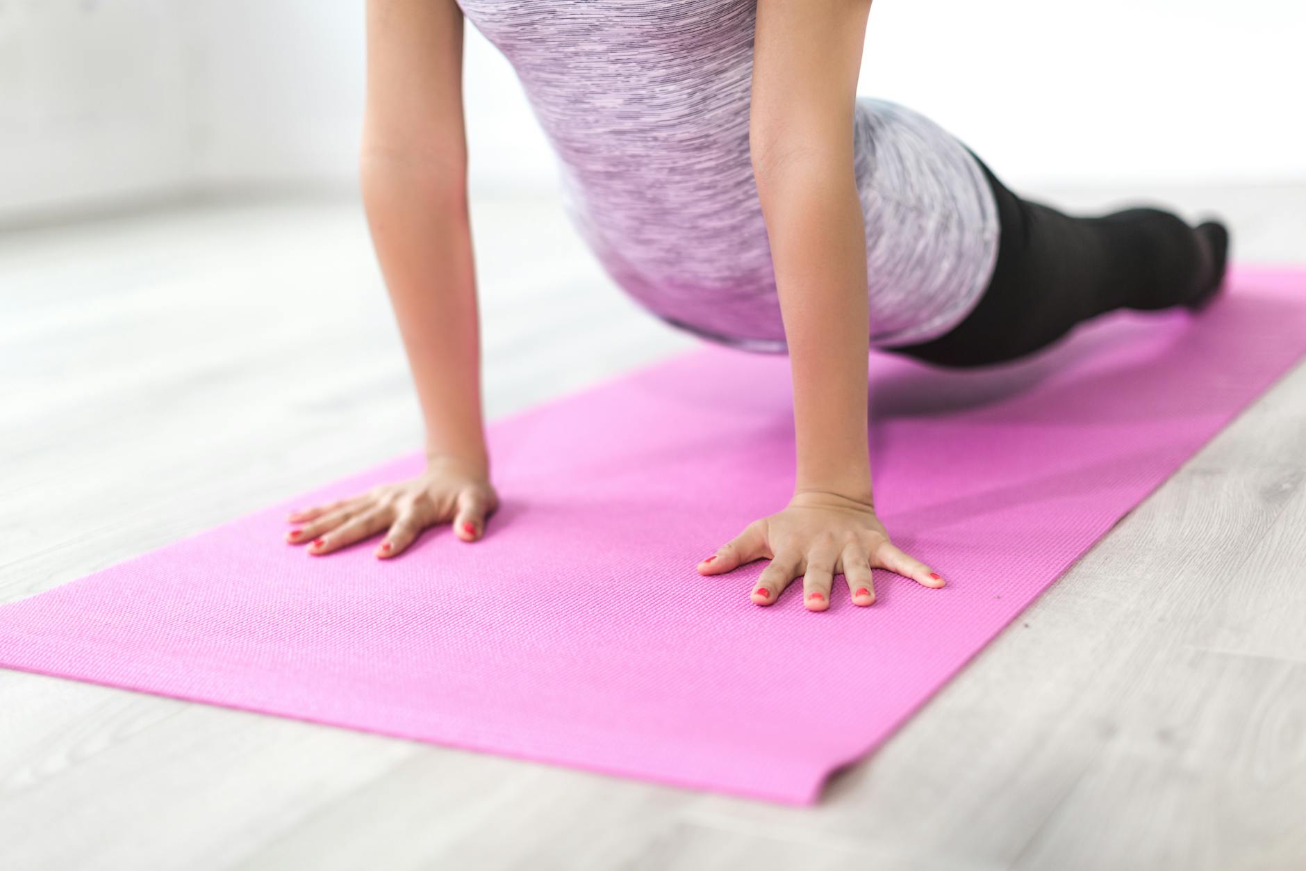 A woman performs a yoga stretch indoors on a pink mat, promoting a healthy lifestyle. - stretching exercises