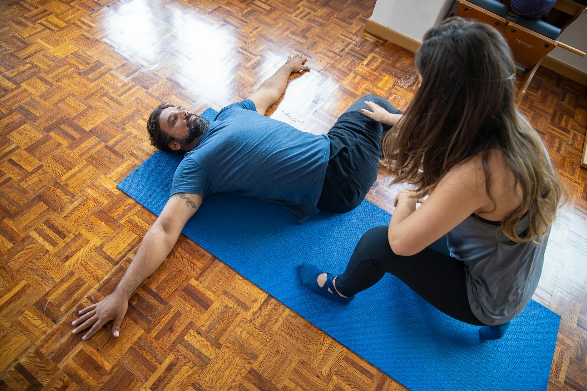 A man and woman engaged in a rehabilitation exercise on a yoga mat indoors. - stretching exercises