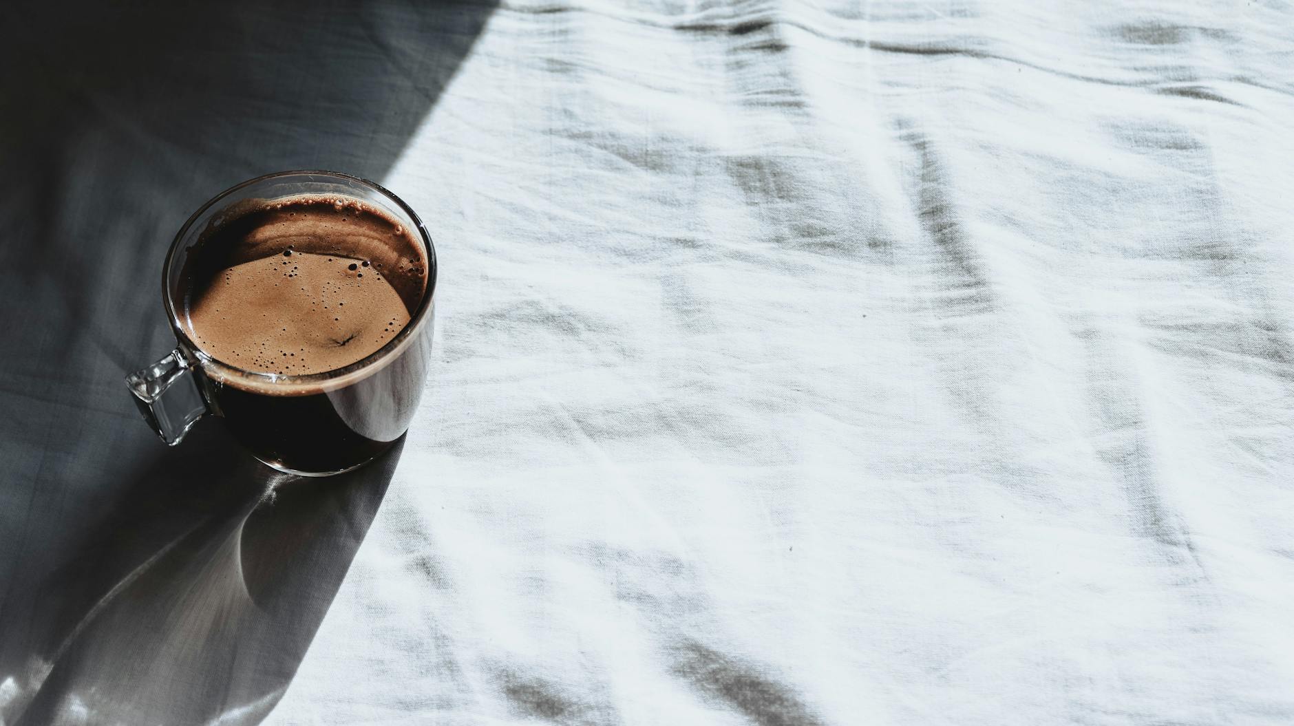 Glass cup of coffee casting shadows on a bright white sheet in natural sunlight. - sunlight mood boost