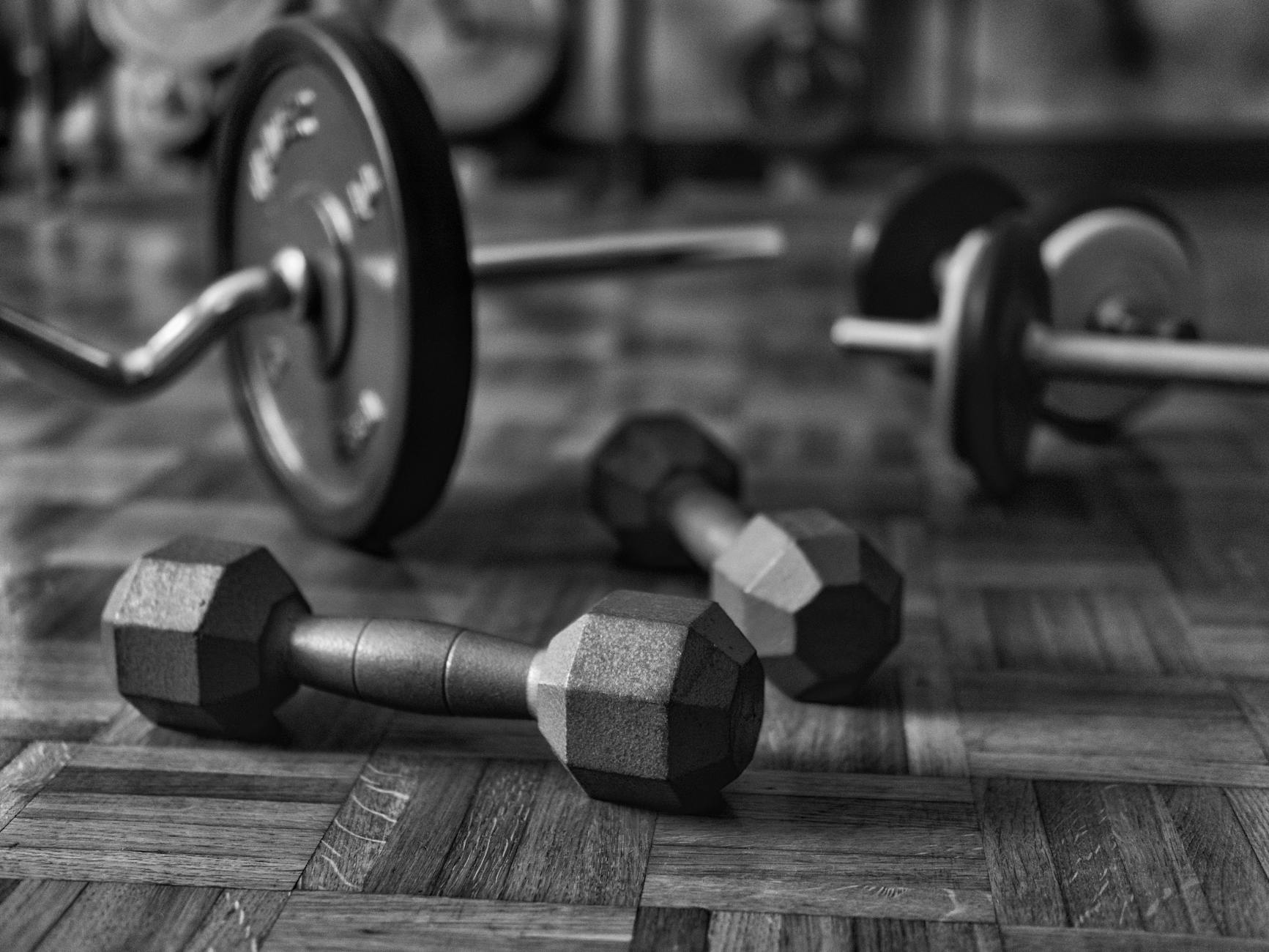 Black and white photo of dumbbells and barbells on a wooden gym floor. - sustainable weight loss