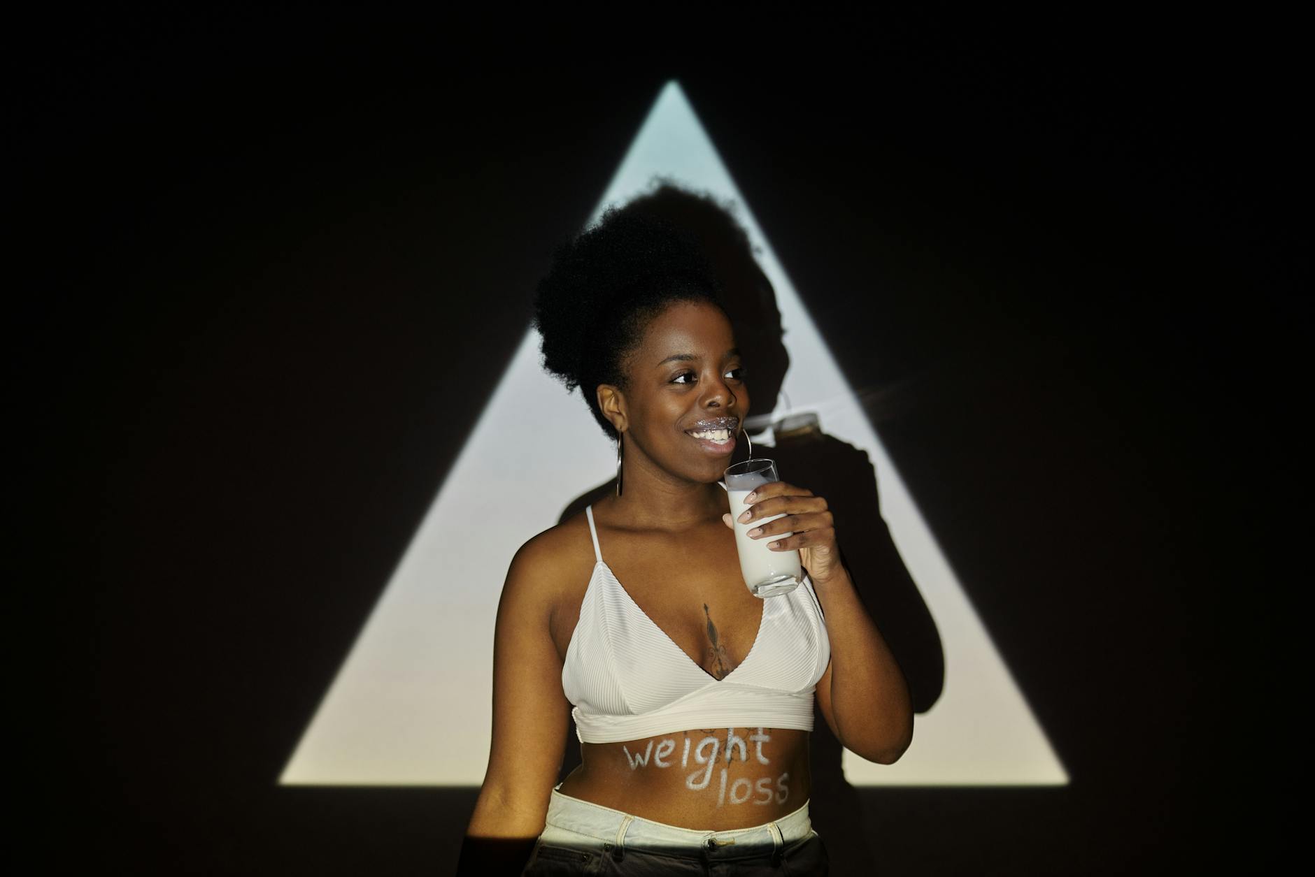 Smiling woman holding a glass of milk against a triangular shadow backdrop, suggesting weight loss concept. - teen weight loss