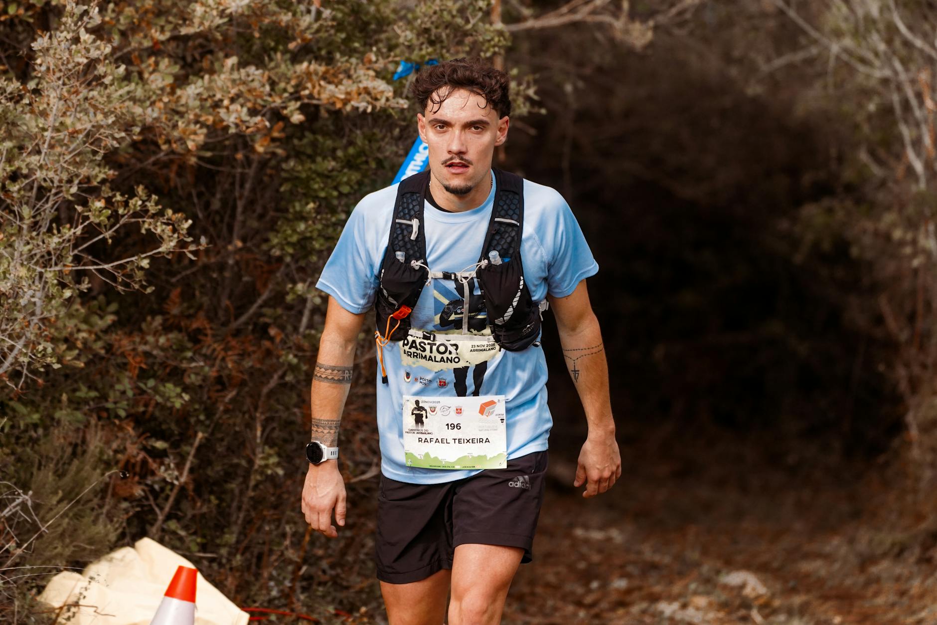 A determined runner in a blue shirt and gear participating in a trail marathon, emerging from a wooded path. - trail running beginners