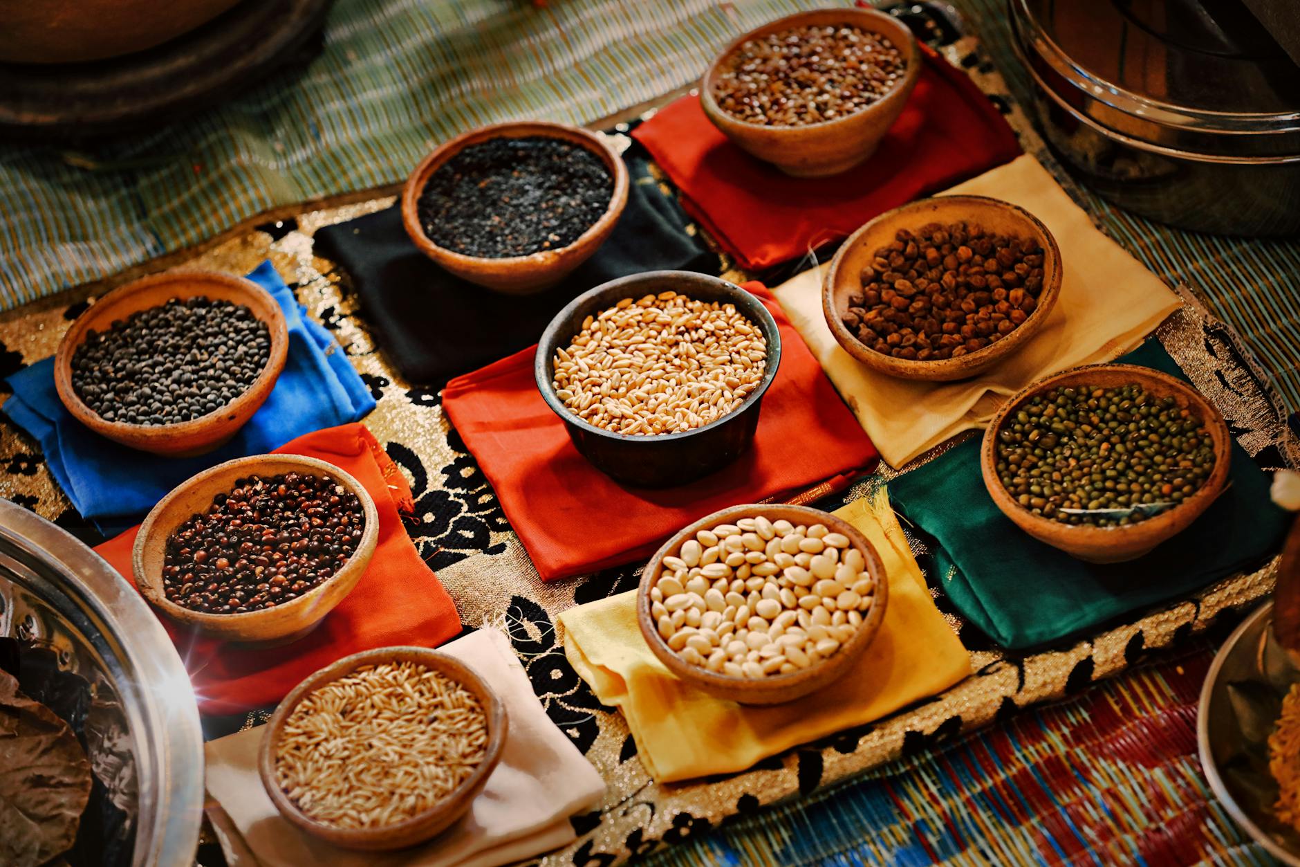 A vibrant assortment of grains and beans in ceramic bowls arranged on colorful textiles, showcasing diverse ingredients. - vegetarian protein sources