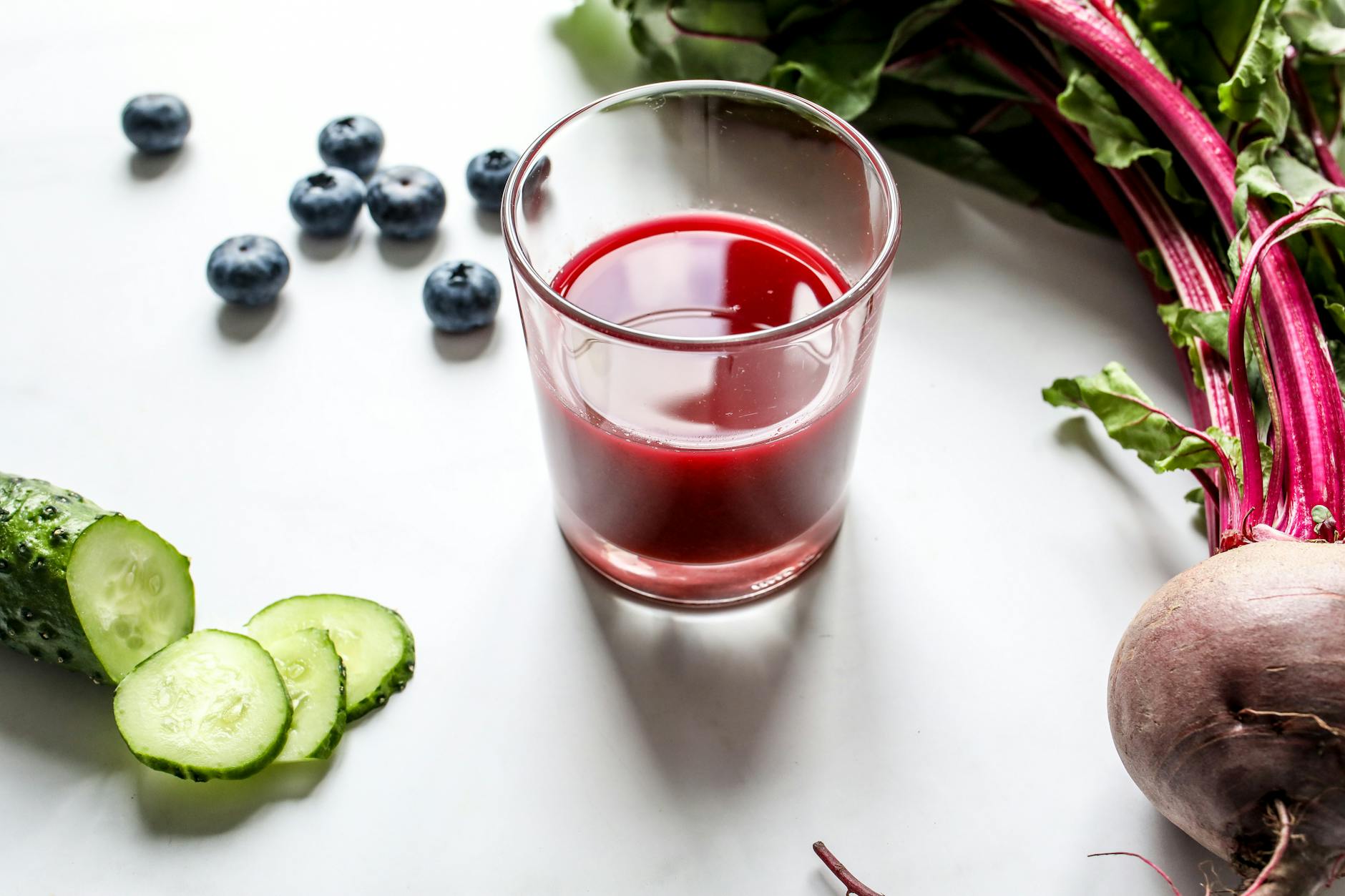 A fresh glass of beetroot juice surrounded by blueberries and cucumber slices. - water fast cleanse