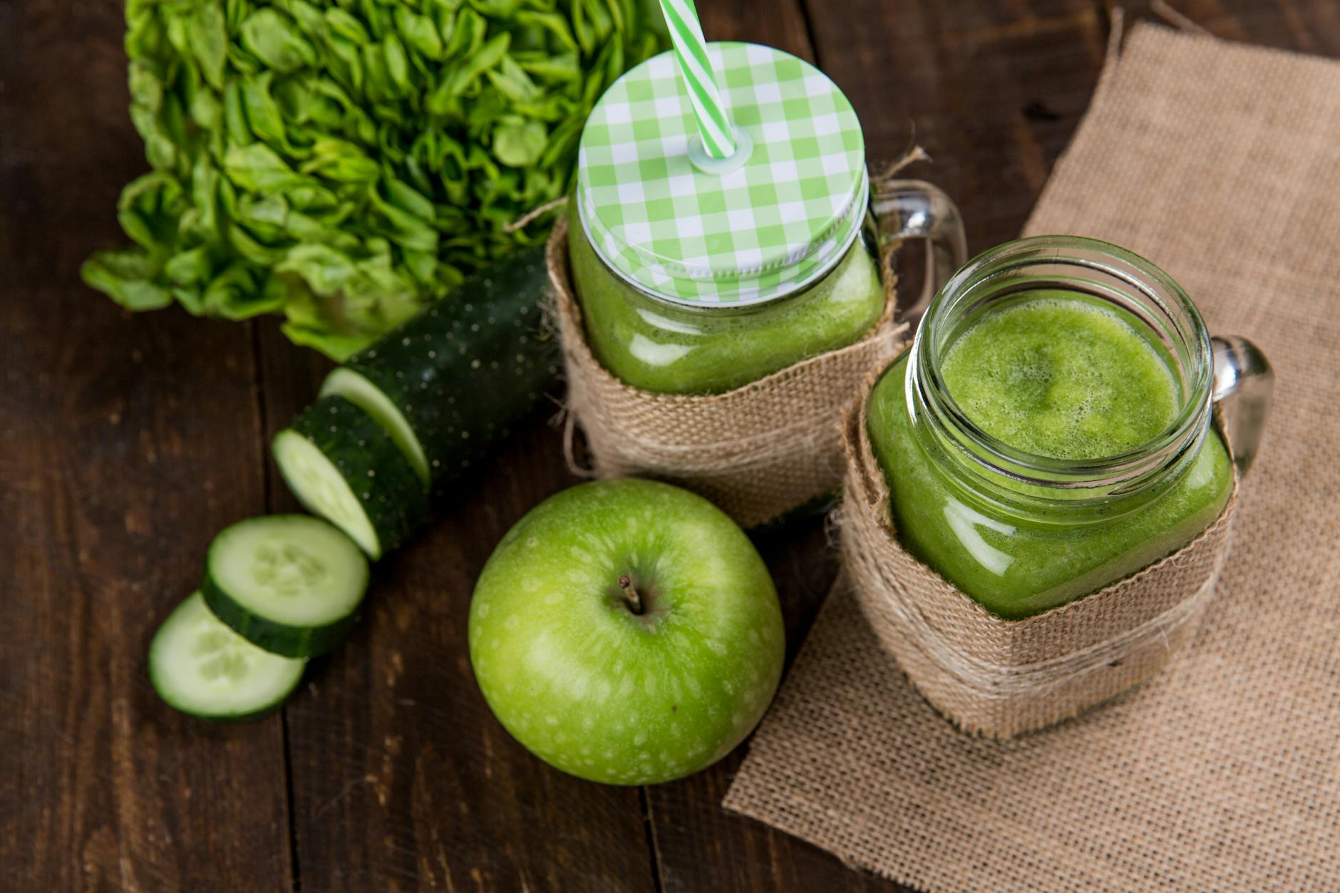 Refreshing green smoothie made with apple, cucumber, and lettuce served in mason jars on wooden background. - water fast cleanse