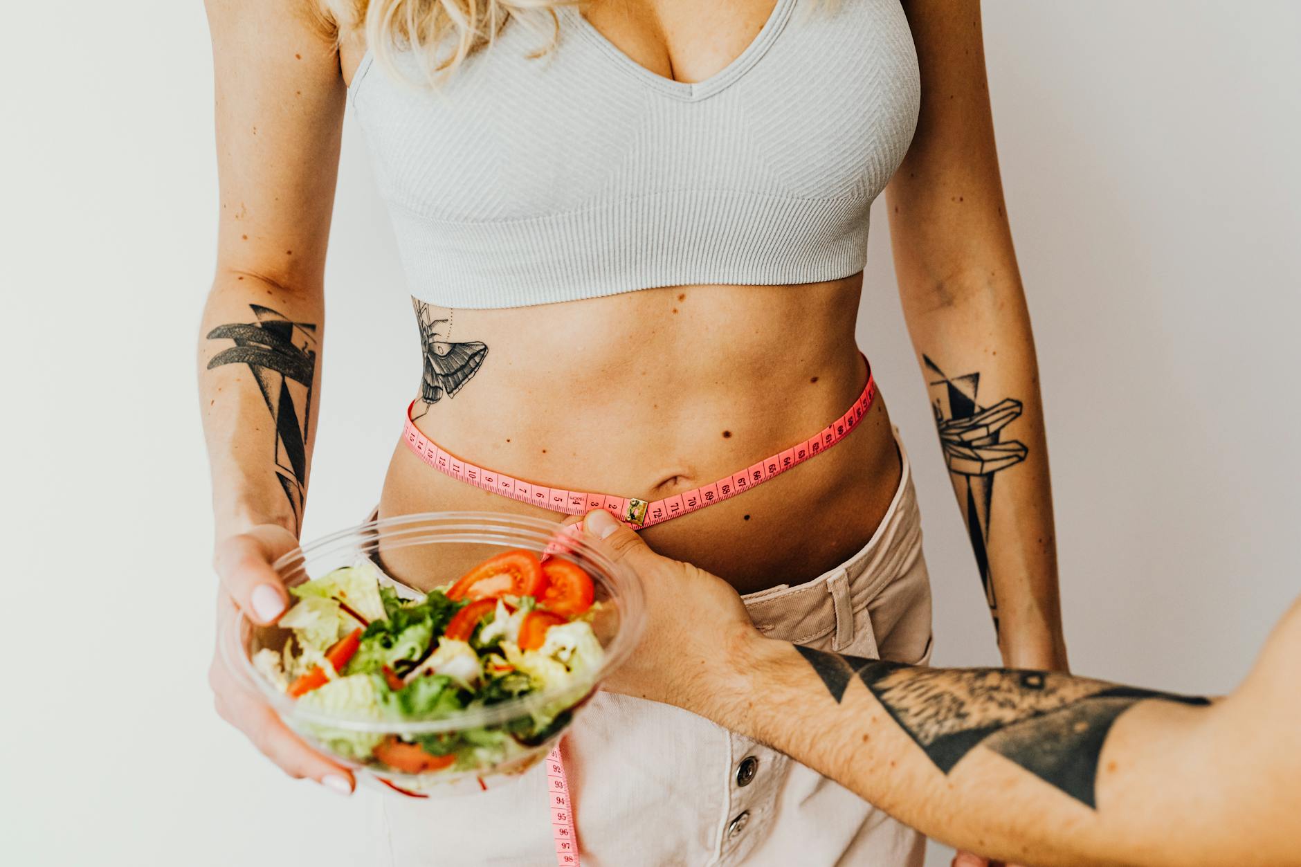 Fit woman measuring waist while holding a healthy salad bowl - weight loss smoothies