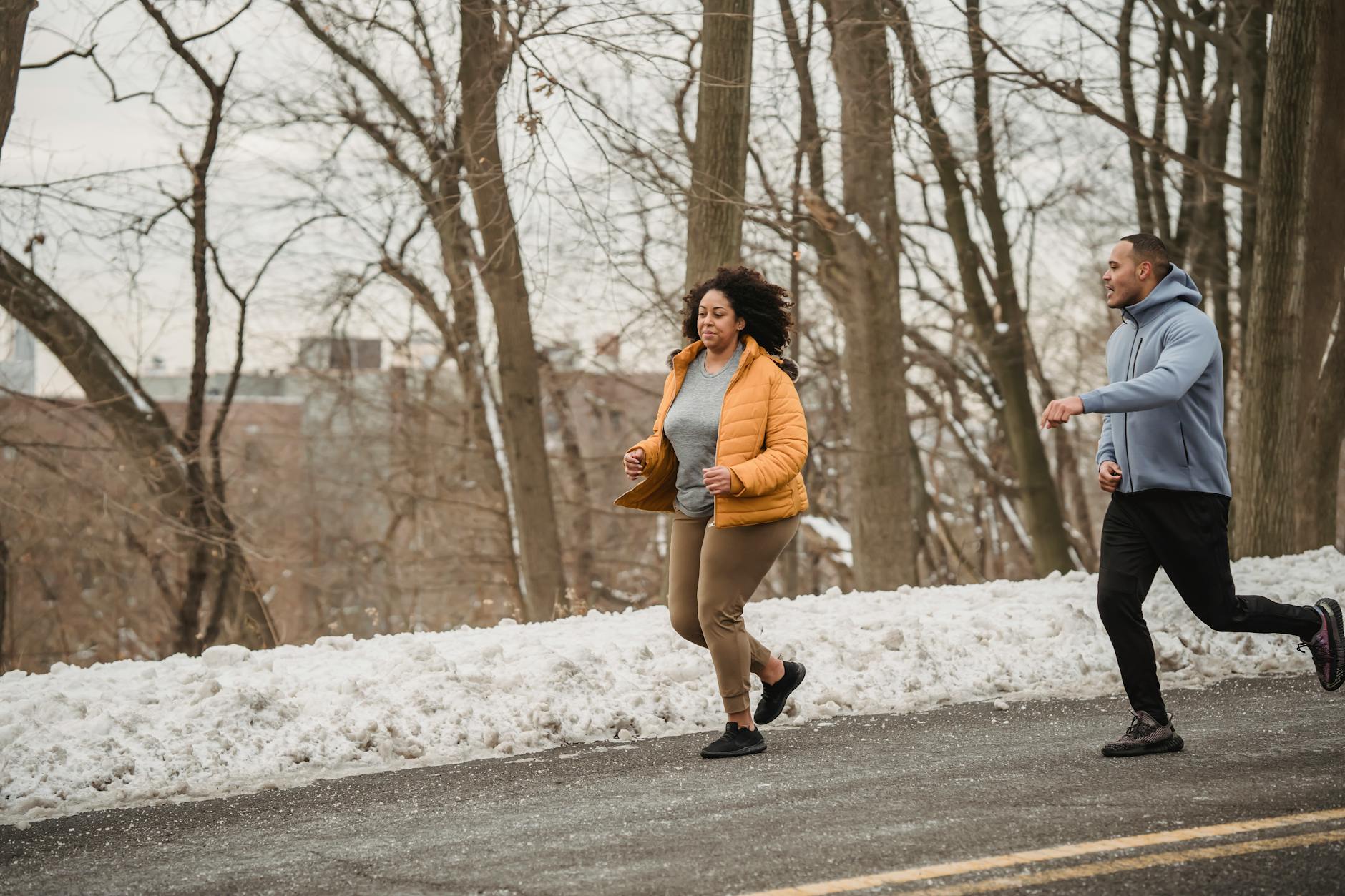 Full body of plus size African American female running with personal instructor on asphalt road during winter training on street - winter wellness slump