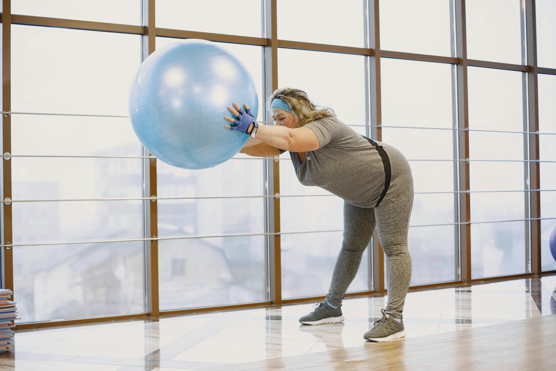 A plus size woman stretches using a fitness ball in a bright gym, promoting wellbeing and body positivity. - yoga for weight loss