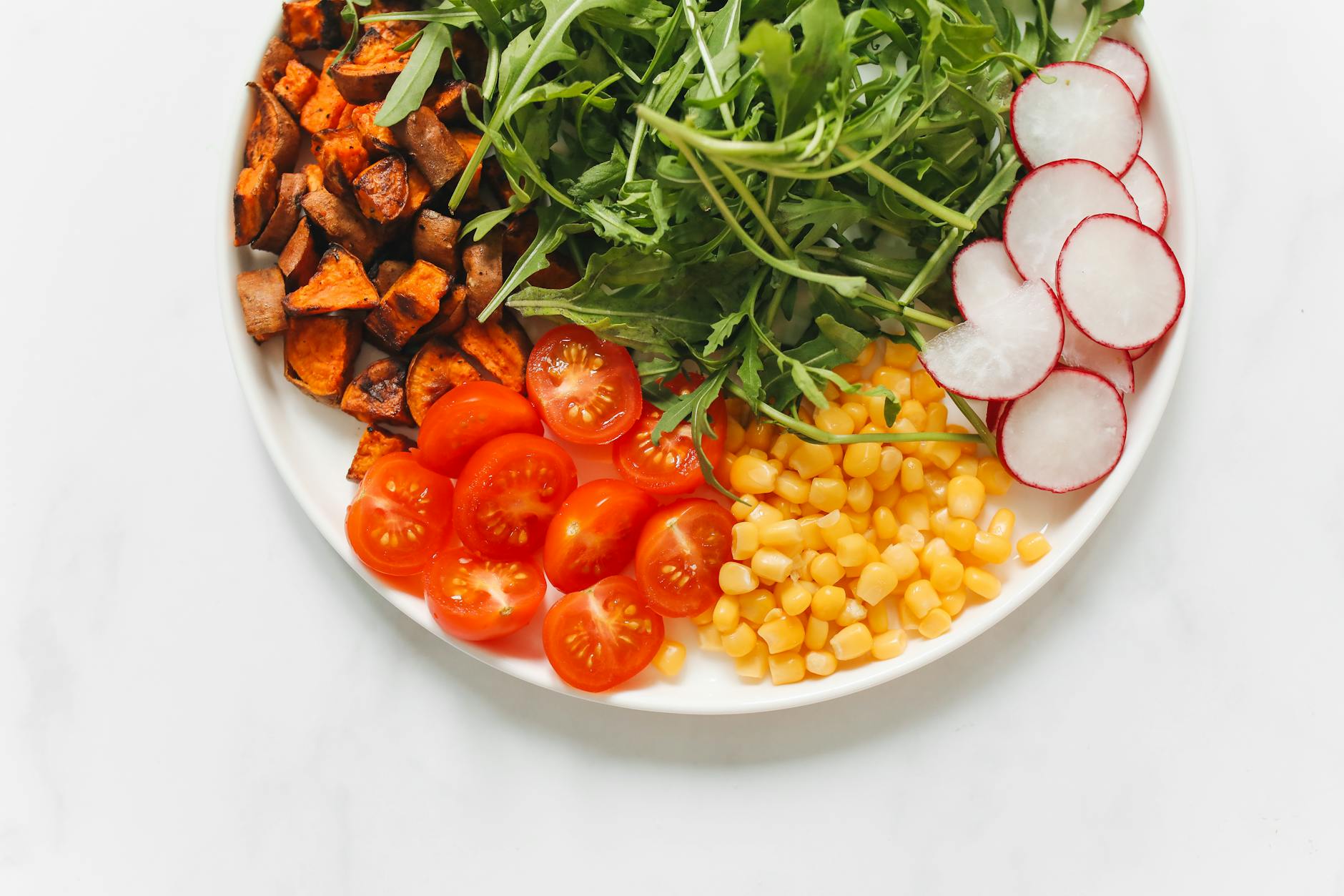 Flat lay of a colorful vegetarian meal with arugula, cherry tomatoes, sweet potatoes, radish, and corn on a plate. - allergy relief diet