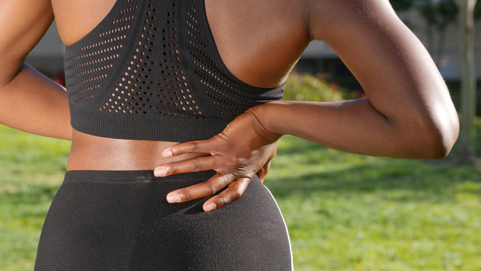 Woman in athletic attire holding her back outside, indicating discomfort or pain. - back pain causes