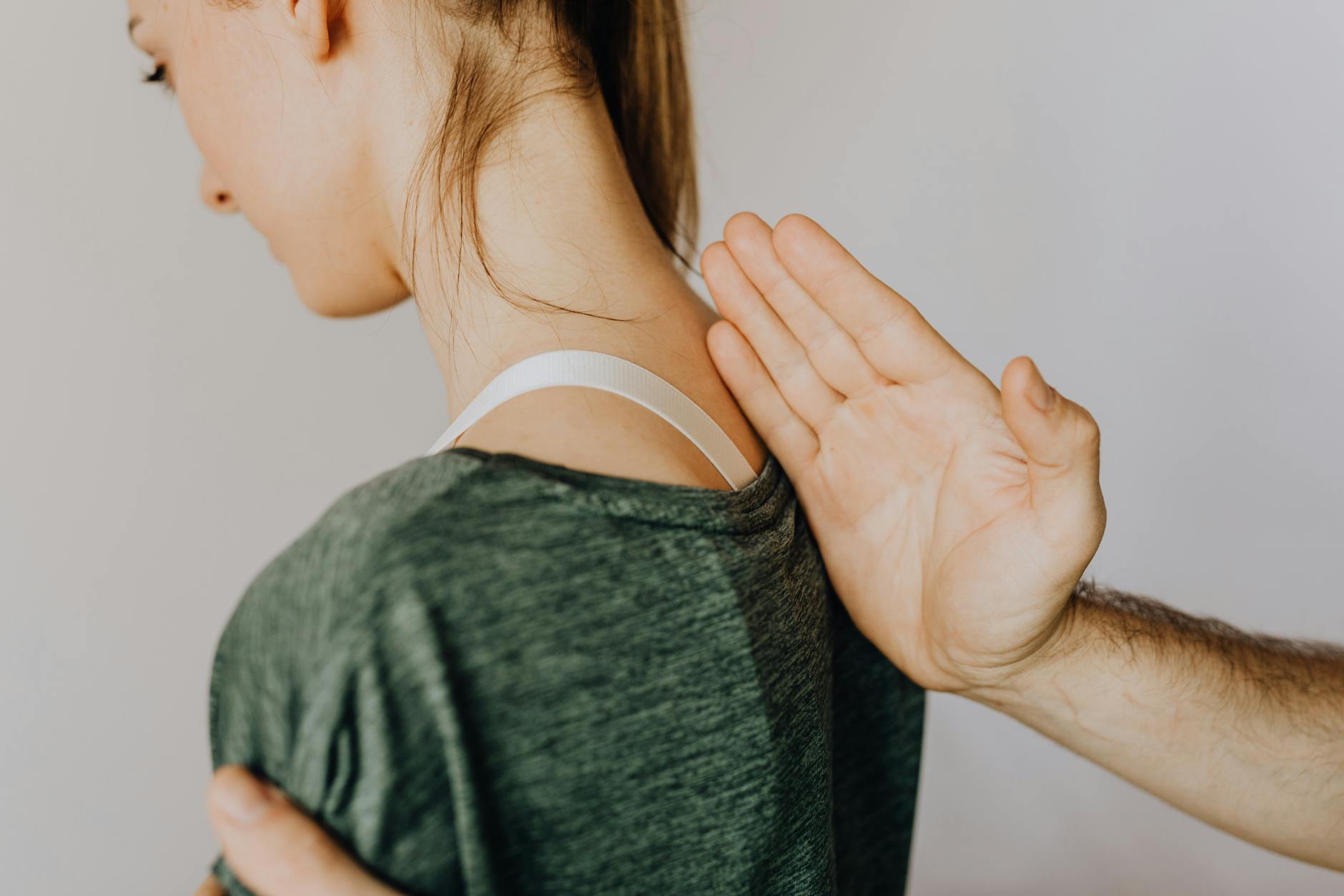 Side view of crop anonymous osteopath examining spine of slim young lady in casual wear near white wall in doctor office - back pain relief