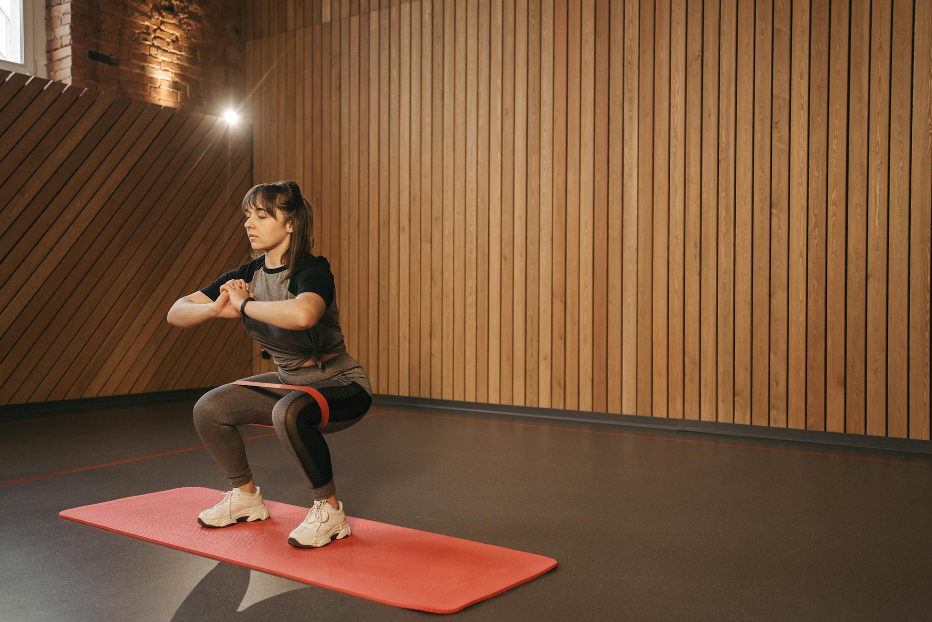 Young woman exercises indoors with resistance band on mat for fitness - beginner strength training