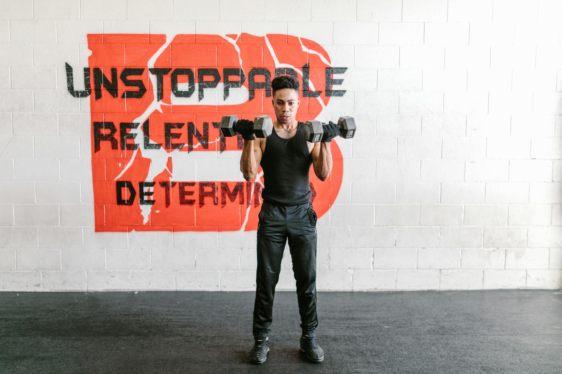 Focused man lifts dumbbells with determination in a gym against motivational graffiti - beginner strength training