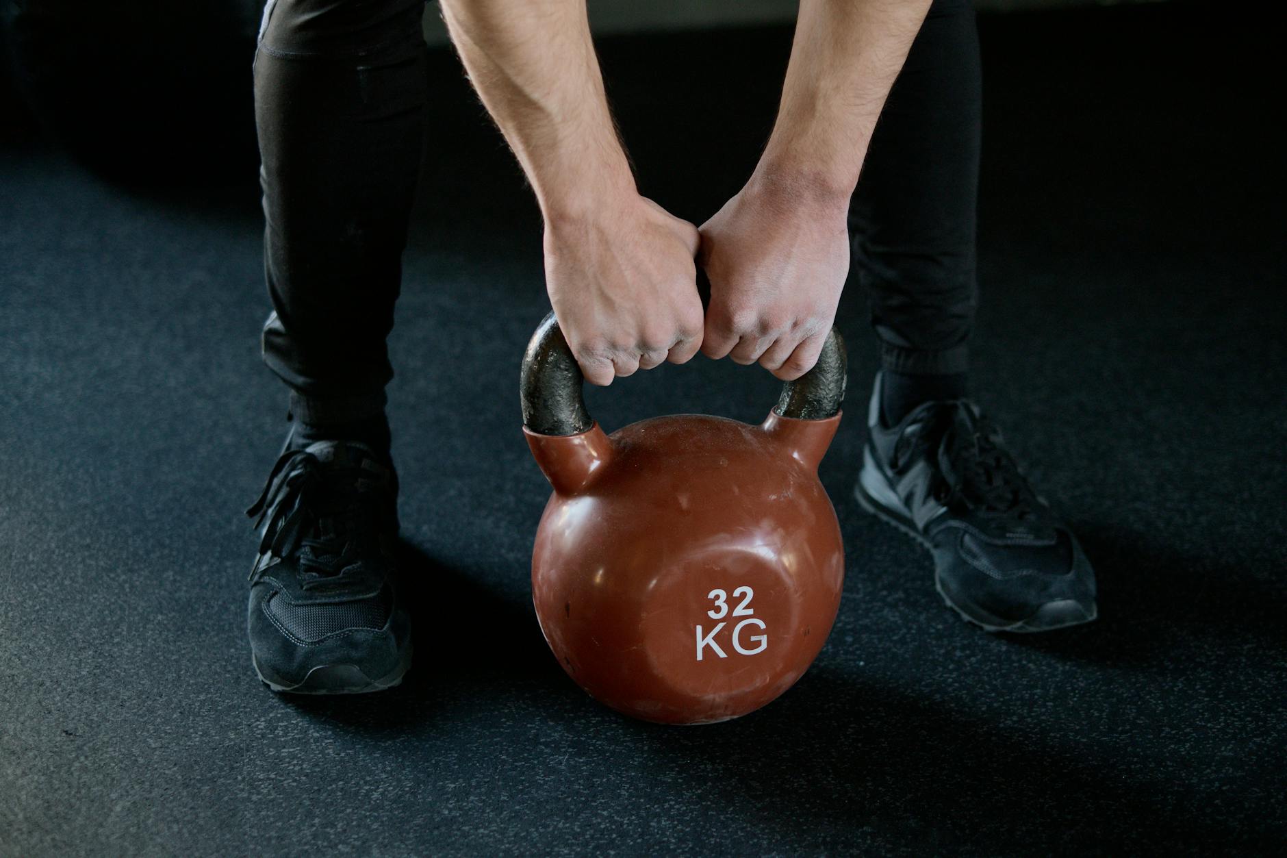A person lifting a 32 kg kettlebell in a gym setting, showcasing strength training. - beginner strength training