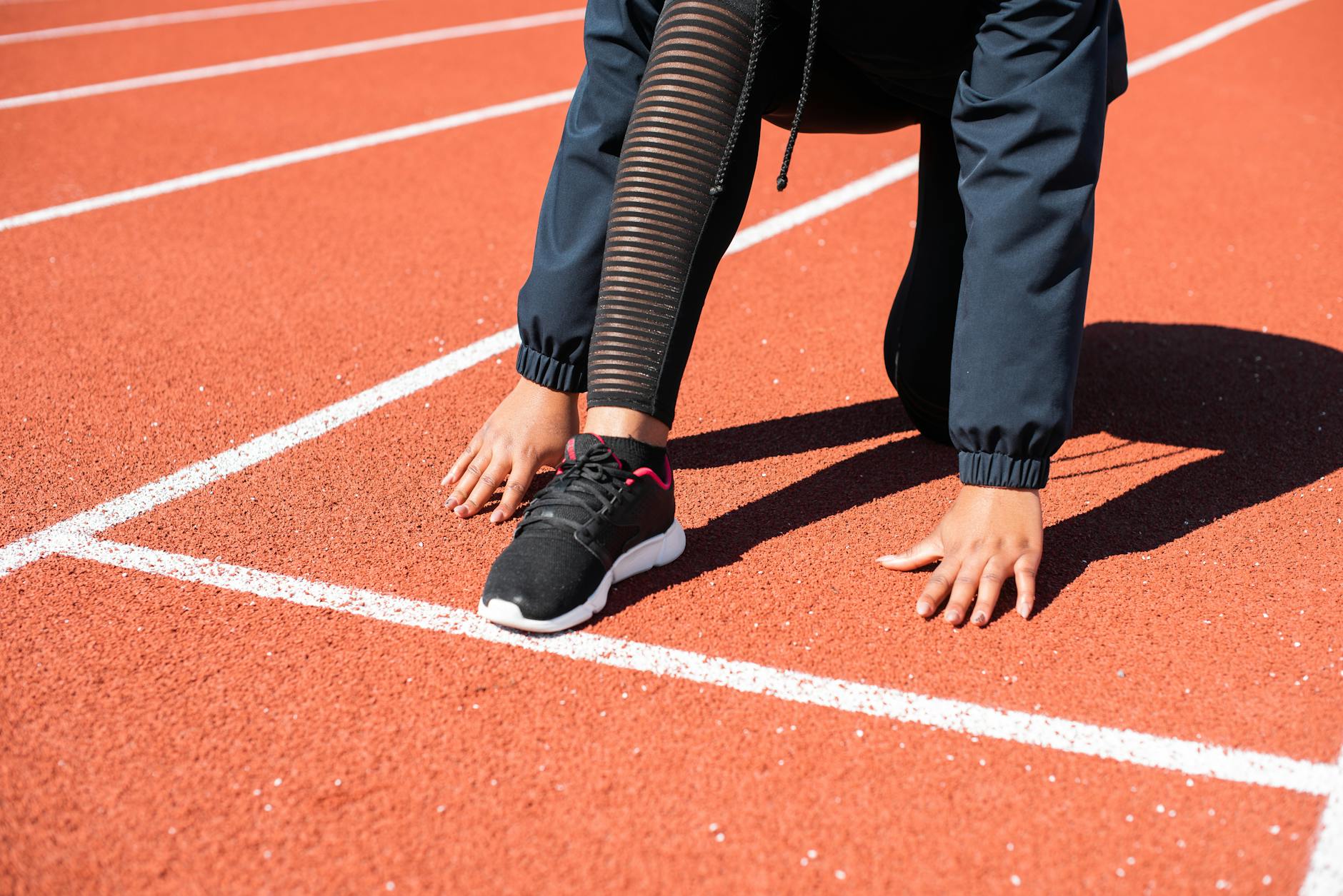 Close-up of a runner crouching at the starting line on an outdoor track. - best running shoes