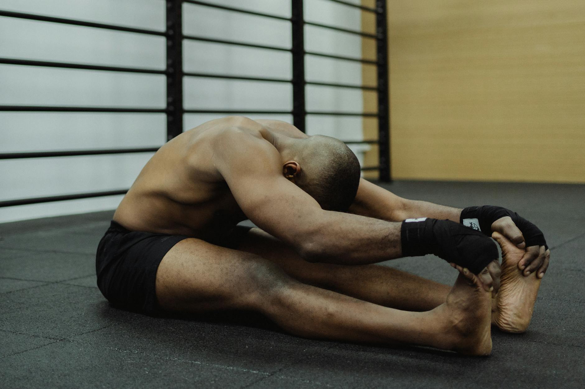 Topless man sitting on gym floor, stretching, showcasing fitness and flexibility. - best stretches
