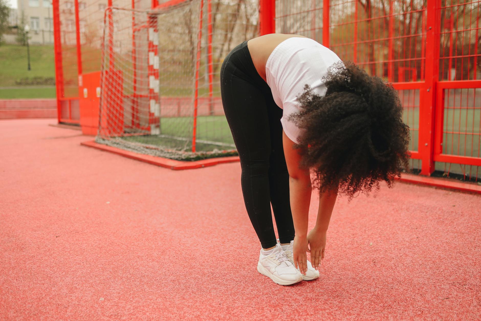 Woman exercising by stretching in a vibrant red outdoor sports court, emphasizing fitness and wellness. - best stretches