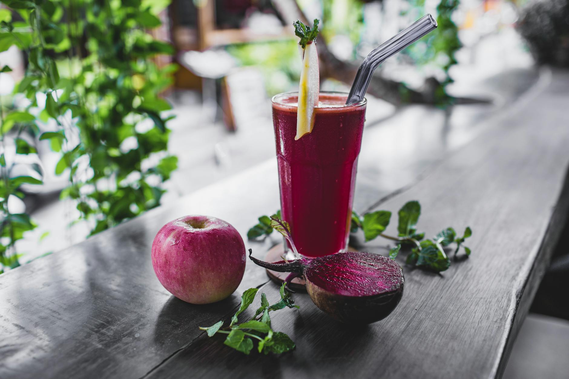 Glass of fresh cold healthy smoothie placed on wooden table on terrace of cafe with whole apple and halved beetroot - body detox diet