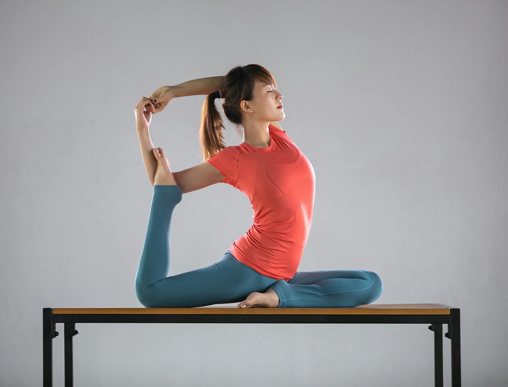 A woman demonstrates an advanced yoga pose on a table indoors, showcasing flexibility and balance. - chair yoga poses