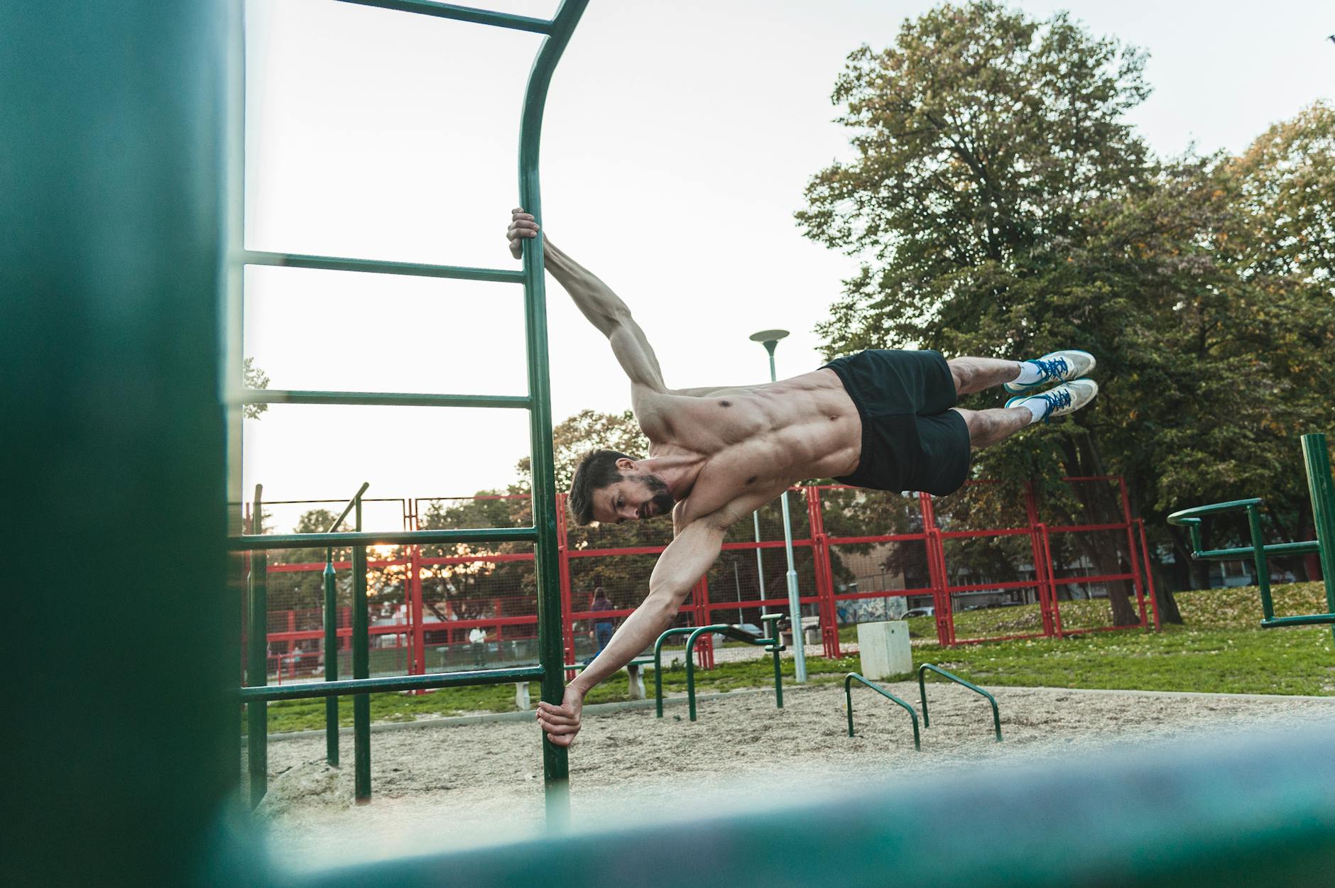 Athletic man demonstrating strength and fitness on outdoor monkey bars during daytime. - core workout day