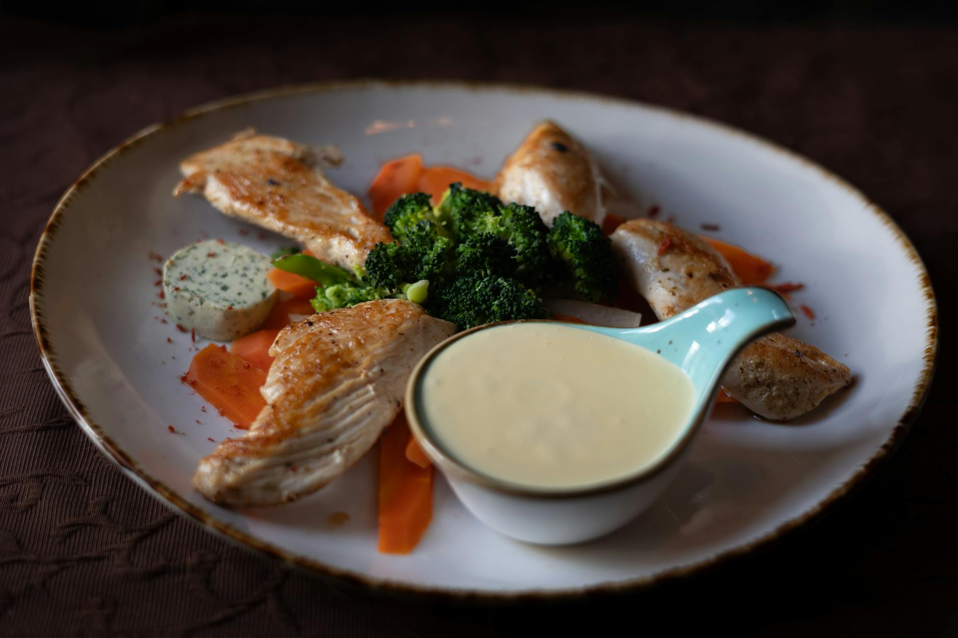 A delectable plate of grilled chicken breast with broccoli, carrots, and a side of creamy sauce. - easy low carb dinners