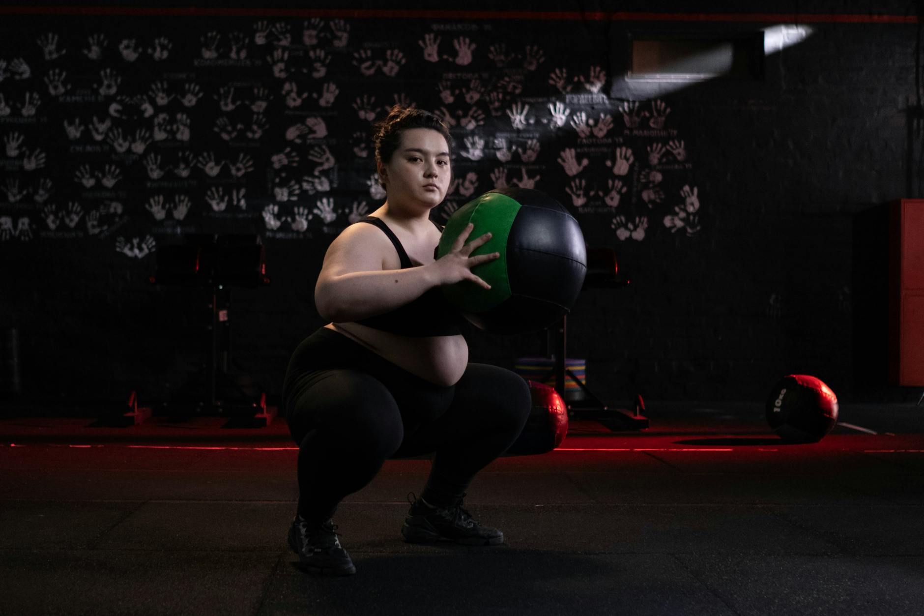 Focused plus size woman performing squats with a medicine ball in a dimly lit gym setting. - full body fat burn