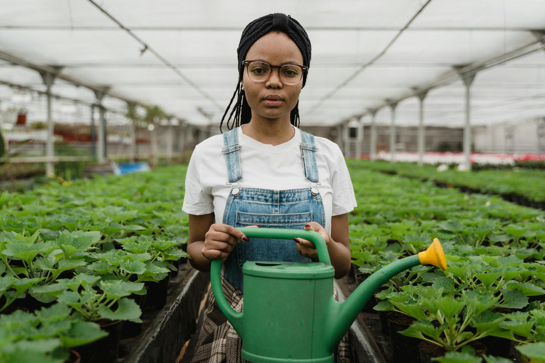 Woman in denim overalls watering plants in a greenhouse, showcasing sustainable gardening. - gardening for health