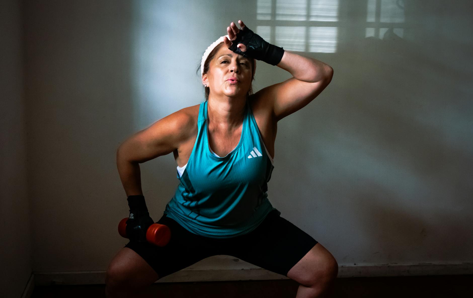 Middle-aged woman working out indoors with red dumbbells, showing strength and determination. - gardening strength training