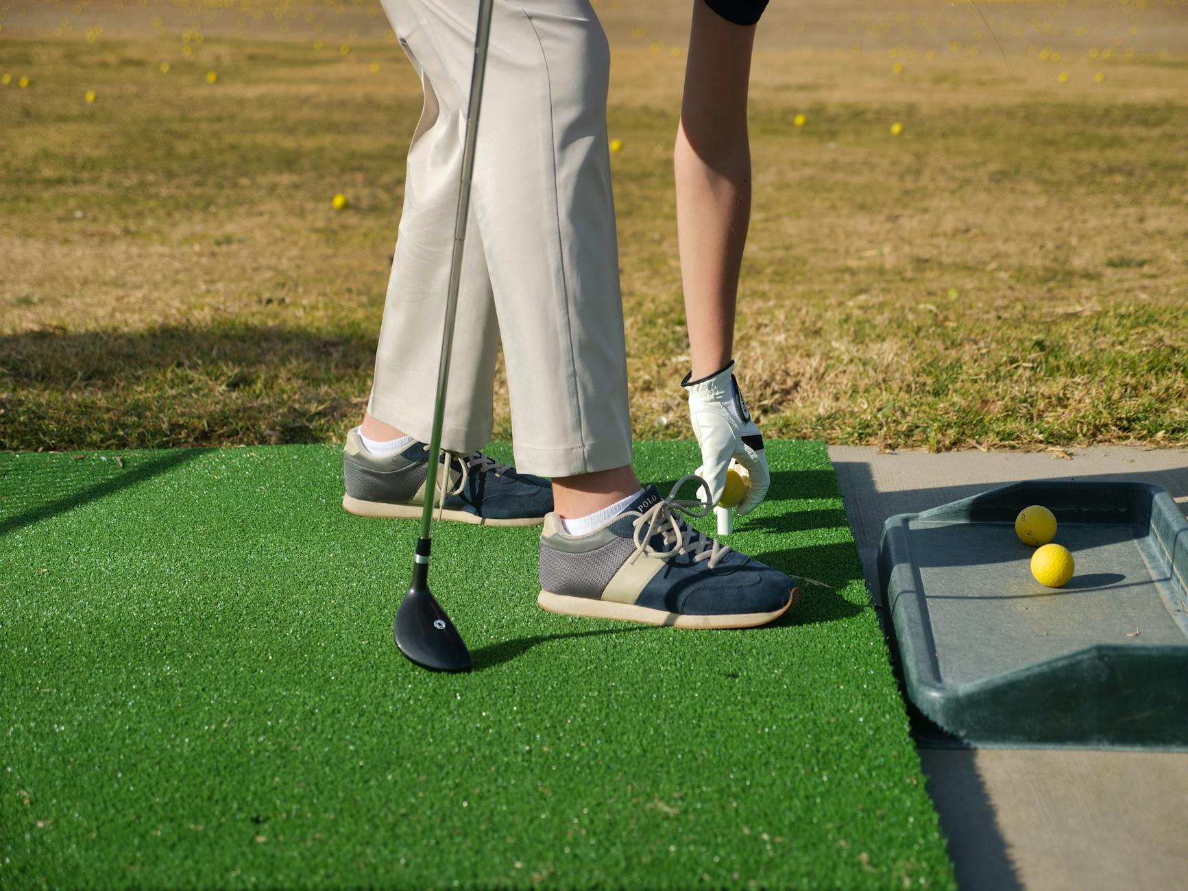 Person placing golf ball on tee at an outdoor driving range for practice. - golf flexibility exercises