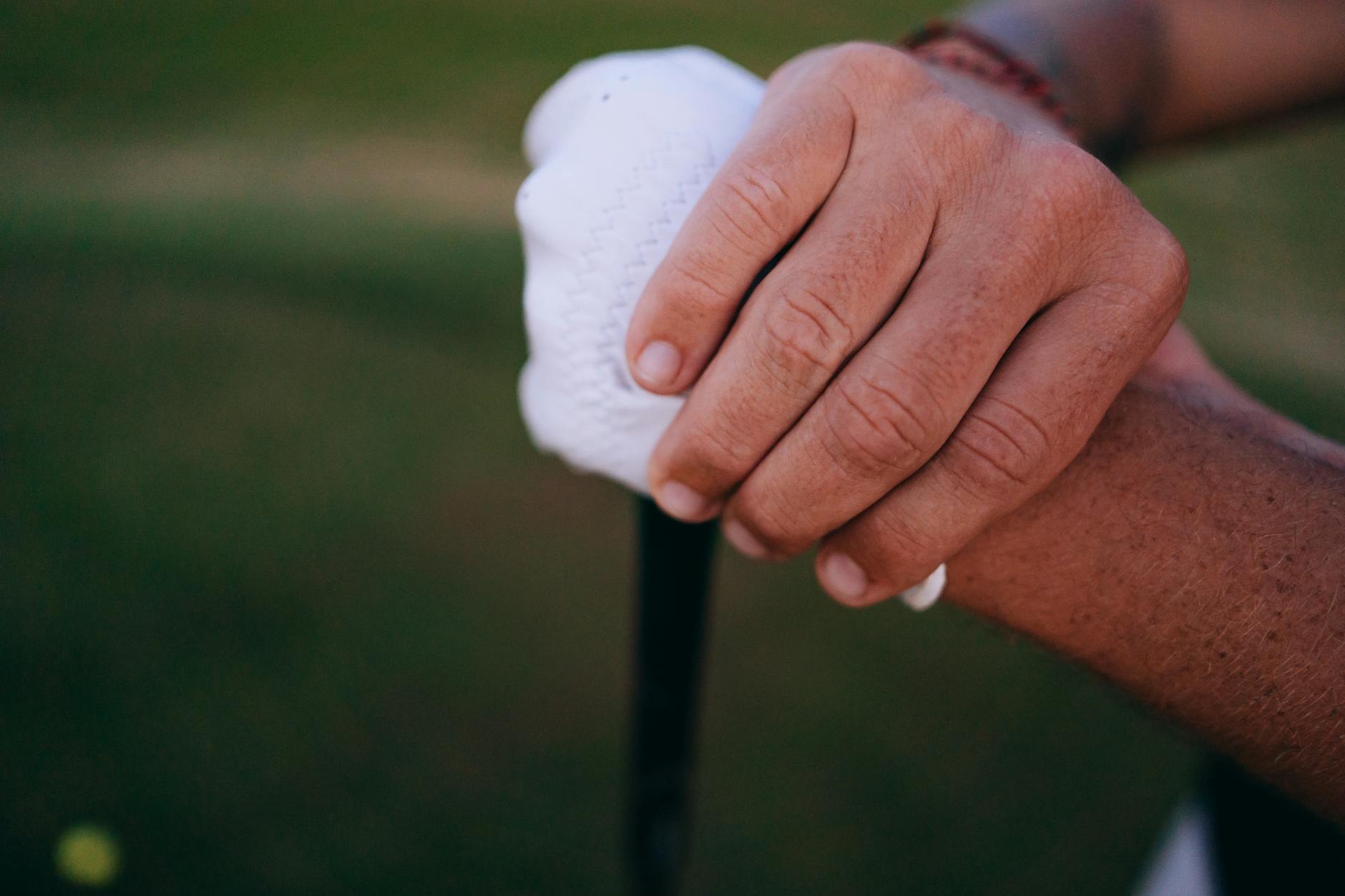 Detailed view of hands gripping a golf club with a white glove outdoors. - golf flexibility exercises