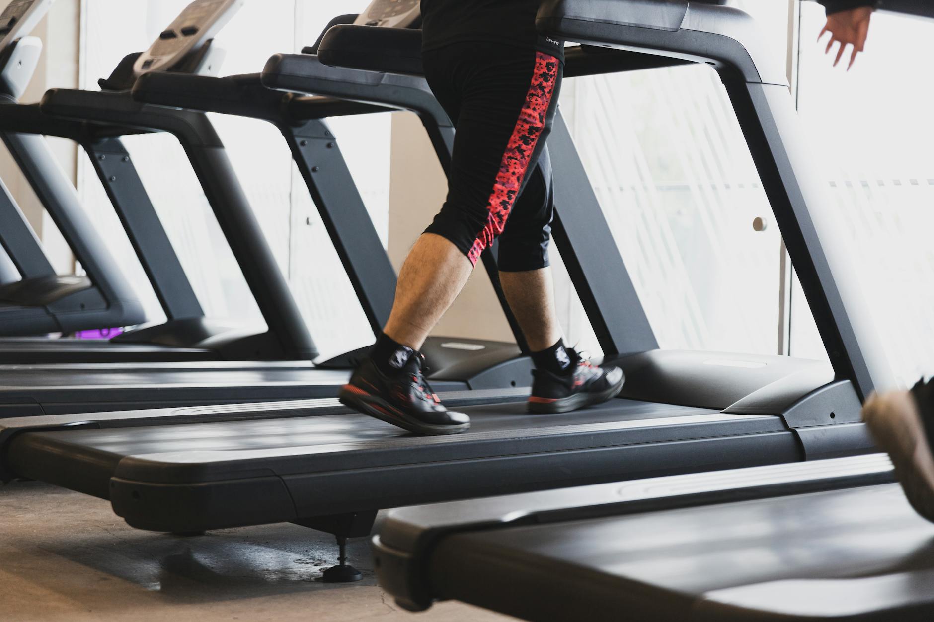 A person walking on a treadmill in a modern gym setting, focusing on fitness. - gym cardio machines