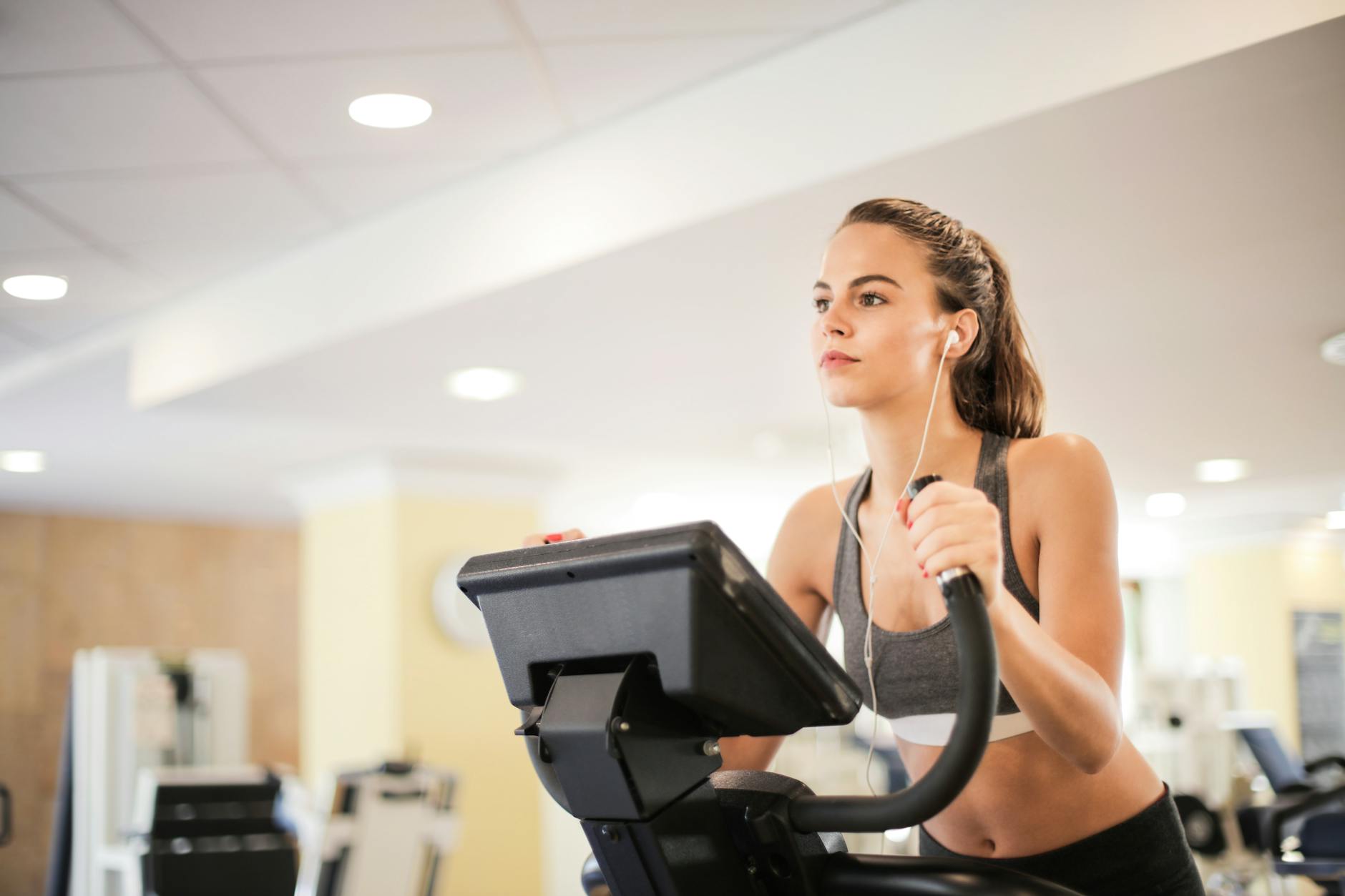Woman in a gym focused on cardio exercise using elliptical machine. Healthy lifestyle and fitness concept. - gym cardio machines