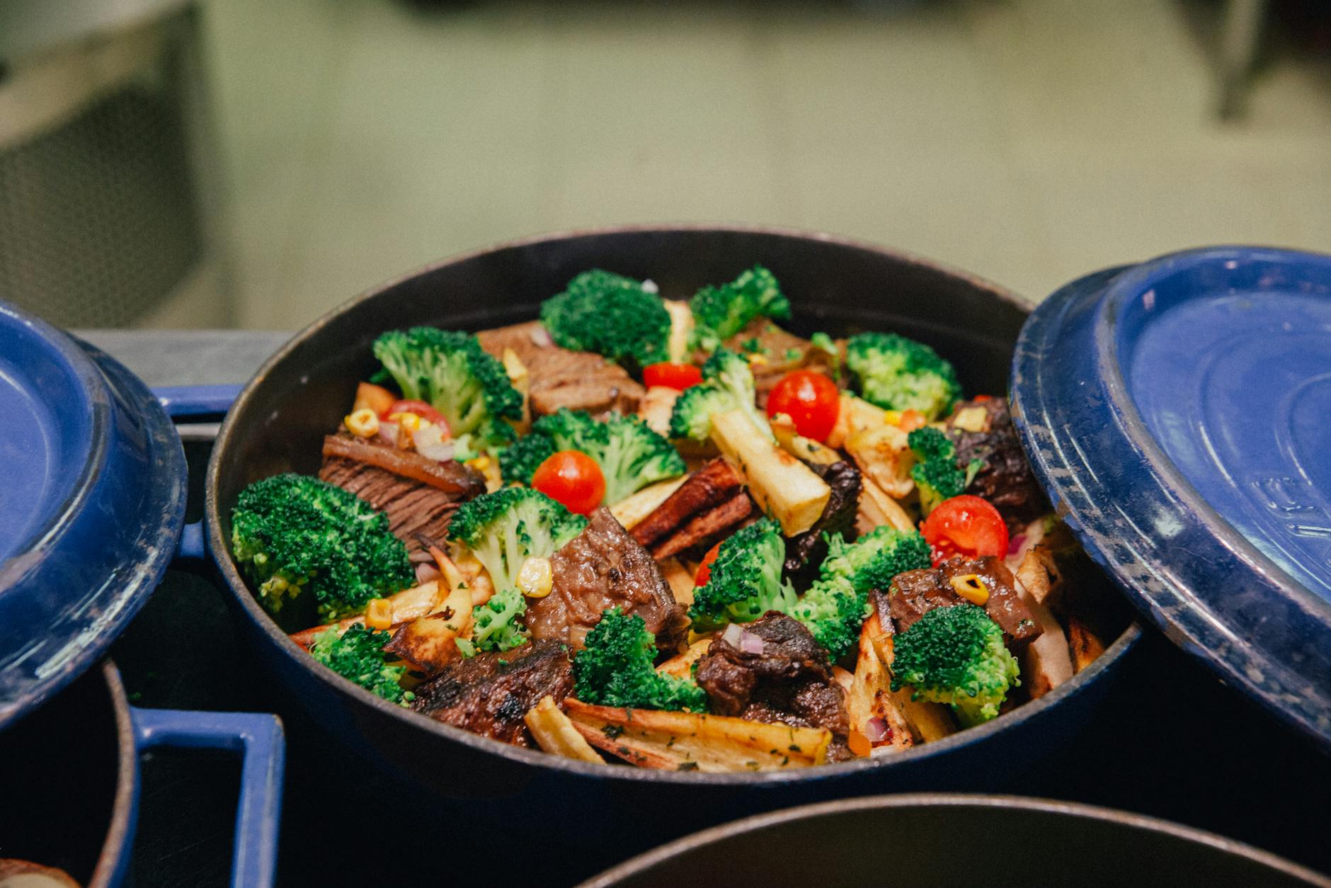 A colorful dish of roasted vegetables and meat in a blue casserole pot, ideal for family dinners. - healthy casserole recipes