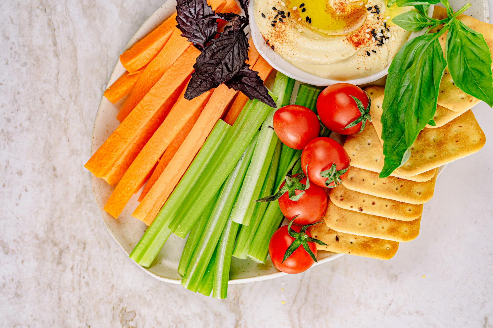 Top view of a fresh vegetable and hummus platter with carrots, celery, cherry tomatoes, and crackers. - healthy spring snacks