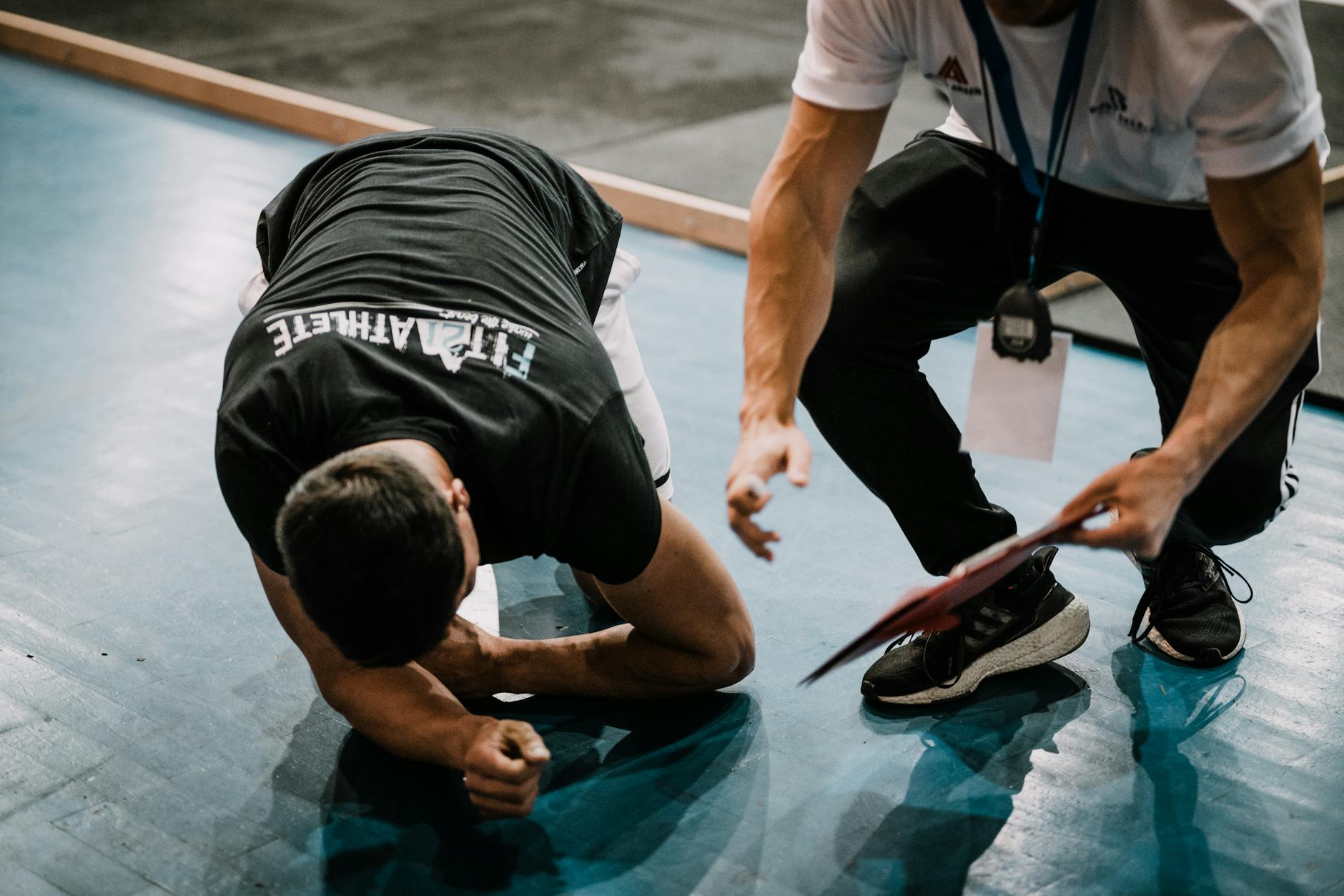 An athlete being assisted by a coach during an indoor training session on a blue floor. - hiit workout plan