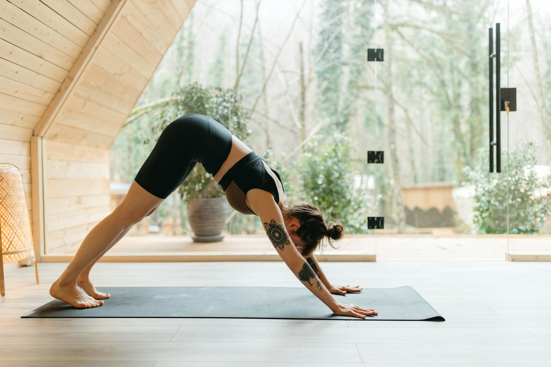 A woman performing the downward dog yoga pose on a mat in a serene indoor setting with natural light. - home wellness retreat