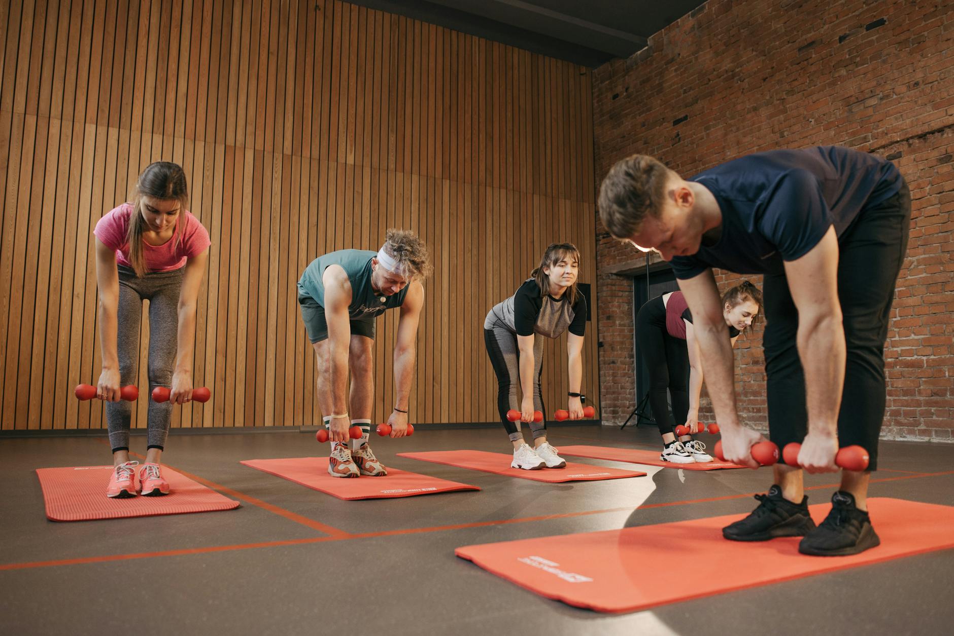 Adults exercising in an indoor fitness class with dumbbells and yoga mats for healthy lifestyle. - interval training fitness